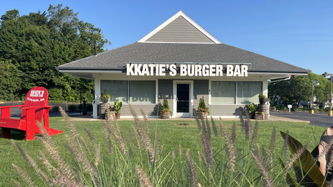 KKatie's Burger Bar with a red Adirondack chair in front, set in a landscaped area, on a sunny day.