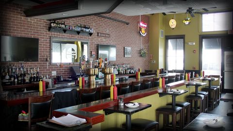 Interior view of a KKatie's Burger Bar with brick walls, bar seating, tables, and a variety of drinks.