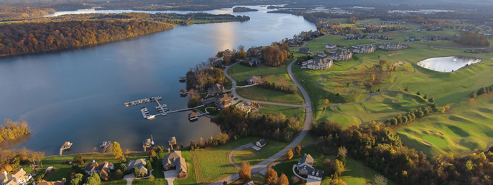 Aerial view of a lakefront community with homes, a marina, and a golf course on a sunny day.