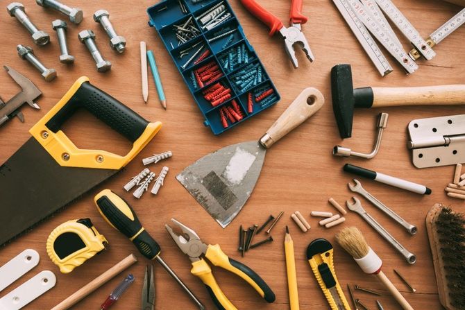 Assorted hand tools and hardware arranged on a wooden surface, including hammers, pliers, screwdrivers, and screws
