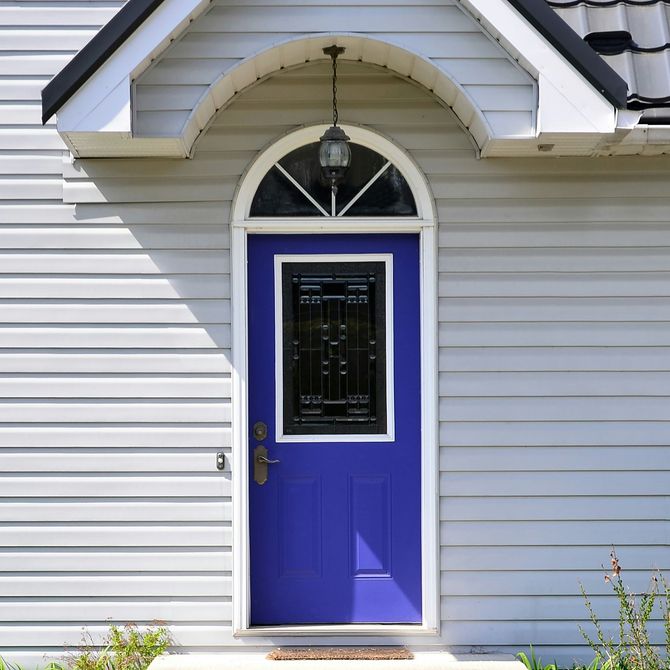 Bright blue front door with a glass panel under an arched porch roof on a white house