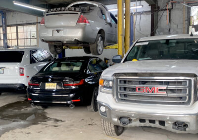 Cars in a repair shop: silver sedan on lift, black car, white SUV, and white GMC truck.