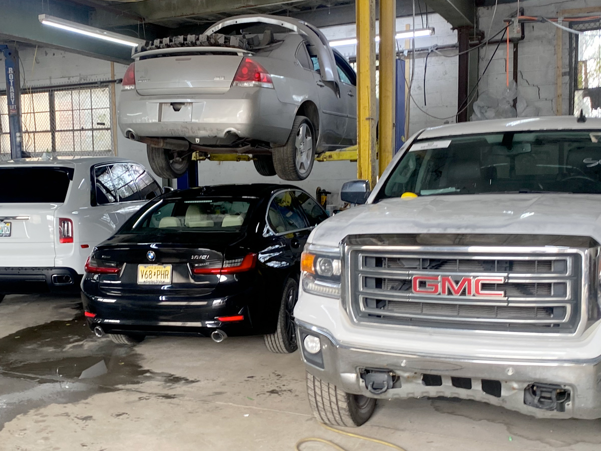 Cars in a repair shop: silver sedan on lift, black car, white truck, white SUV.