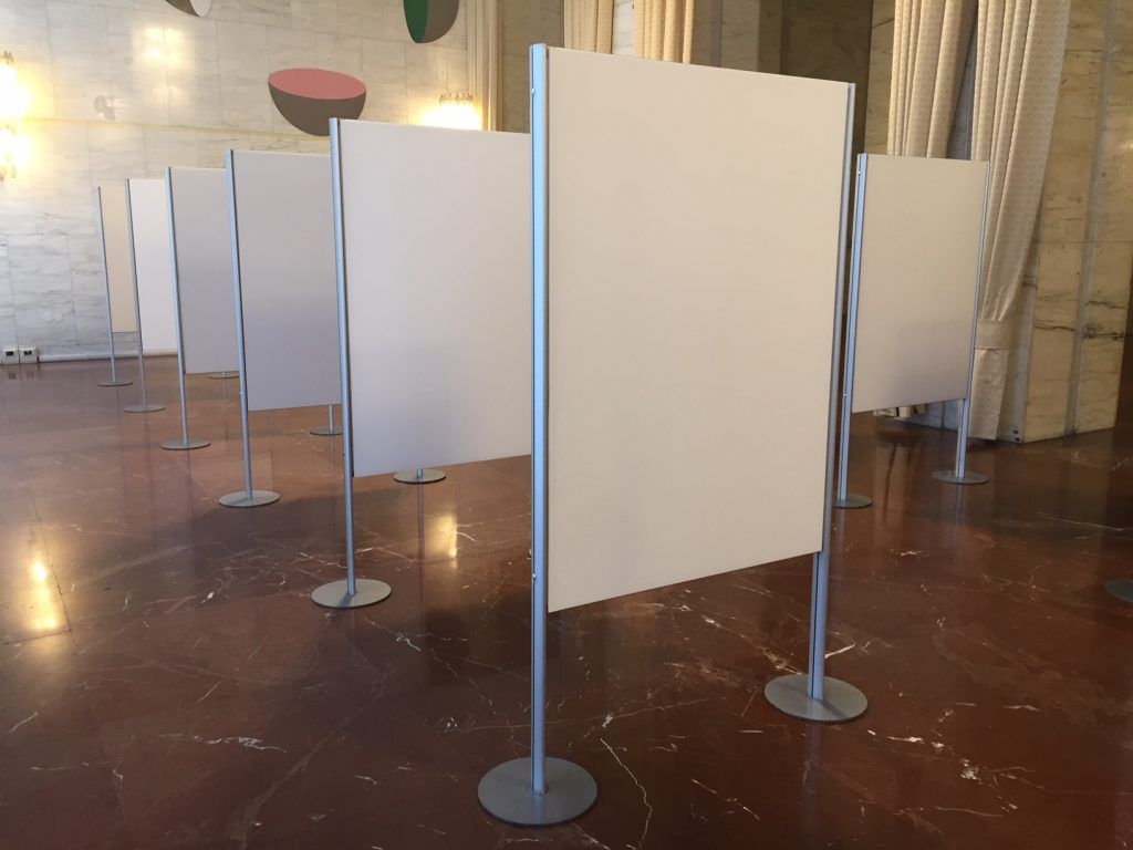 Pannelli espositivi bianchi su supporti metallici in una stanza con pavimento in legno lucido