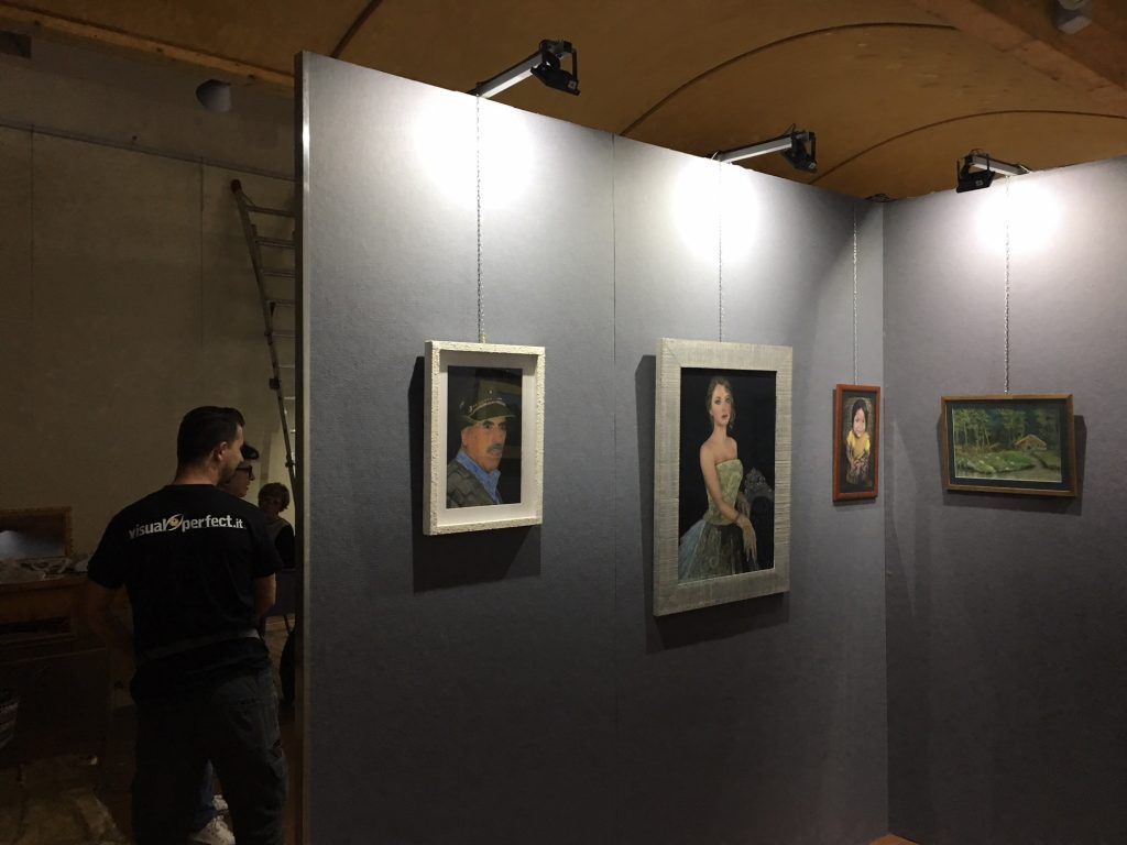 Mostra in galleria d'arte con dipinti incorniciati su pannelli grigi e un visitatore che passa di lì.