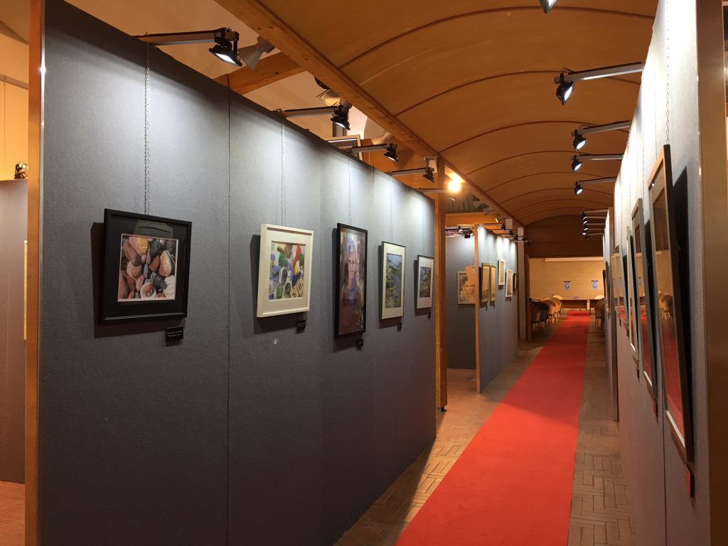 Corridoio di una galleria d'arte con quadri incorniciati su pareti scure e un tappeto rosso sotto calde luci del soffitto.