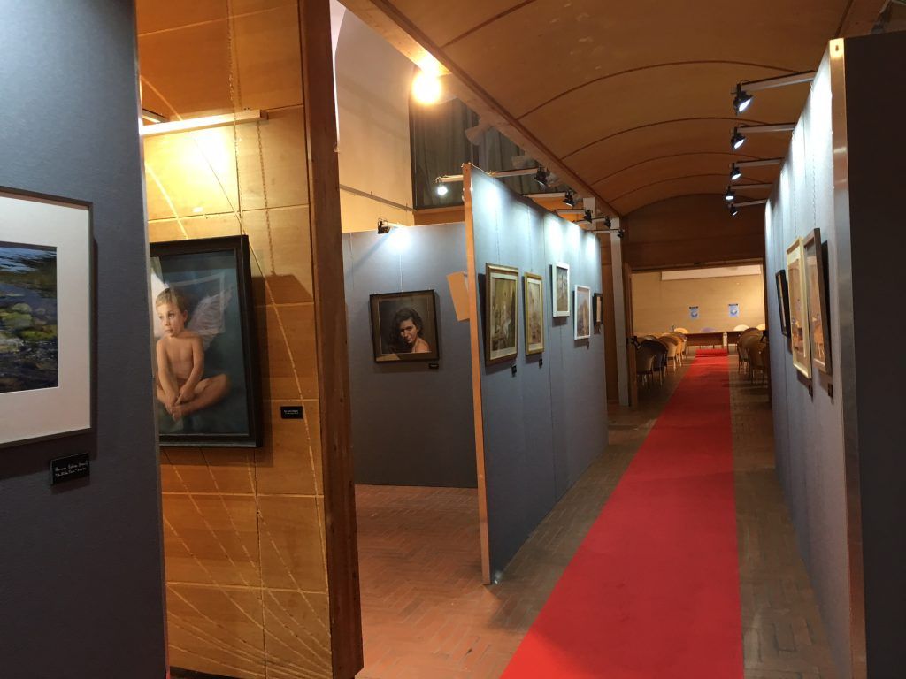 Corridoio della galleria d'arte con quadri incorniciati, pareti blu, luci calde e un tappeto rosso.