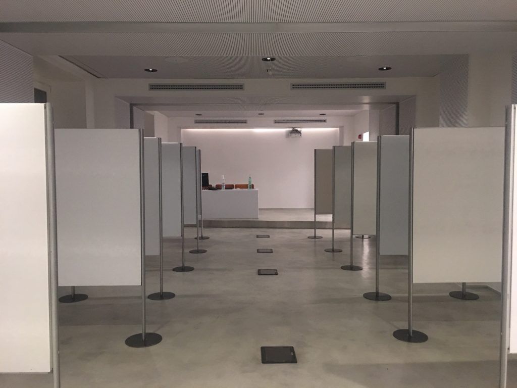 Galleria interna vuota con pannelli espositivi bianchi su piedistalli in una stanza spaziosa.