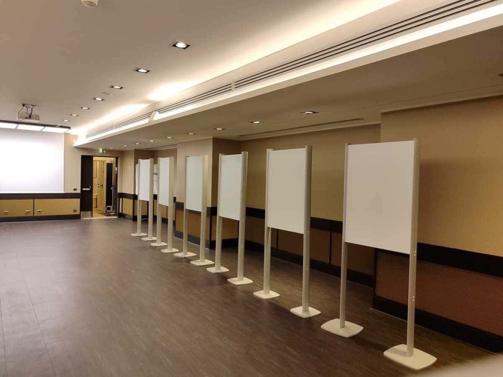 Sala conferenze vuota con una fila di lavagne bianche su supporti e luci a soffitto.