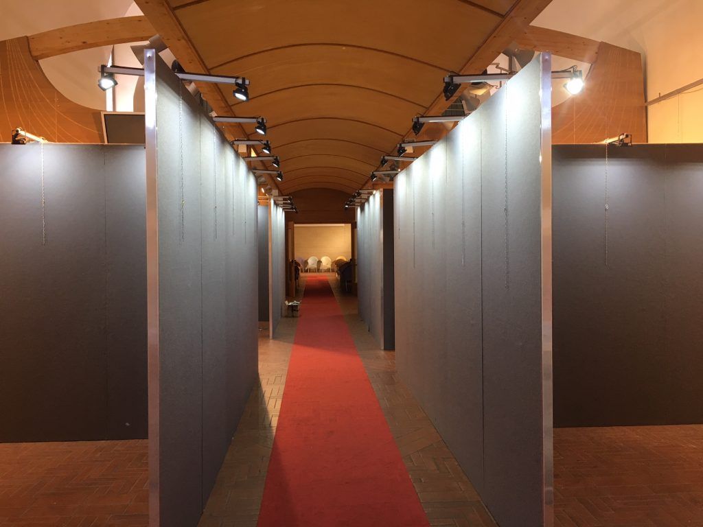 Lungo corridoio con pareti divisorie grigie e moquette rossa sotto un soffitto a volta in legno.