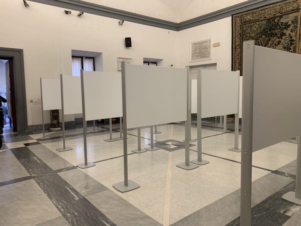 Galleria museale con pannelli espositivi vuoti su supporti metallici in una stanza piastrellata.