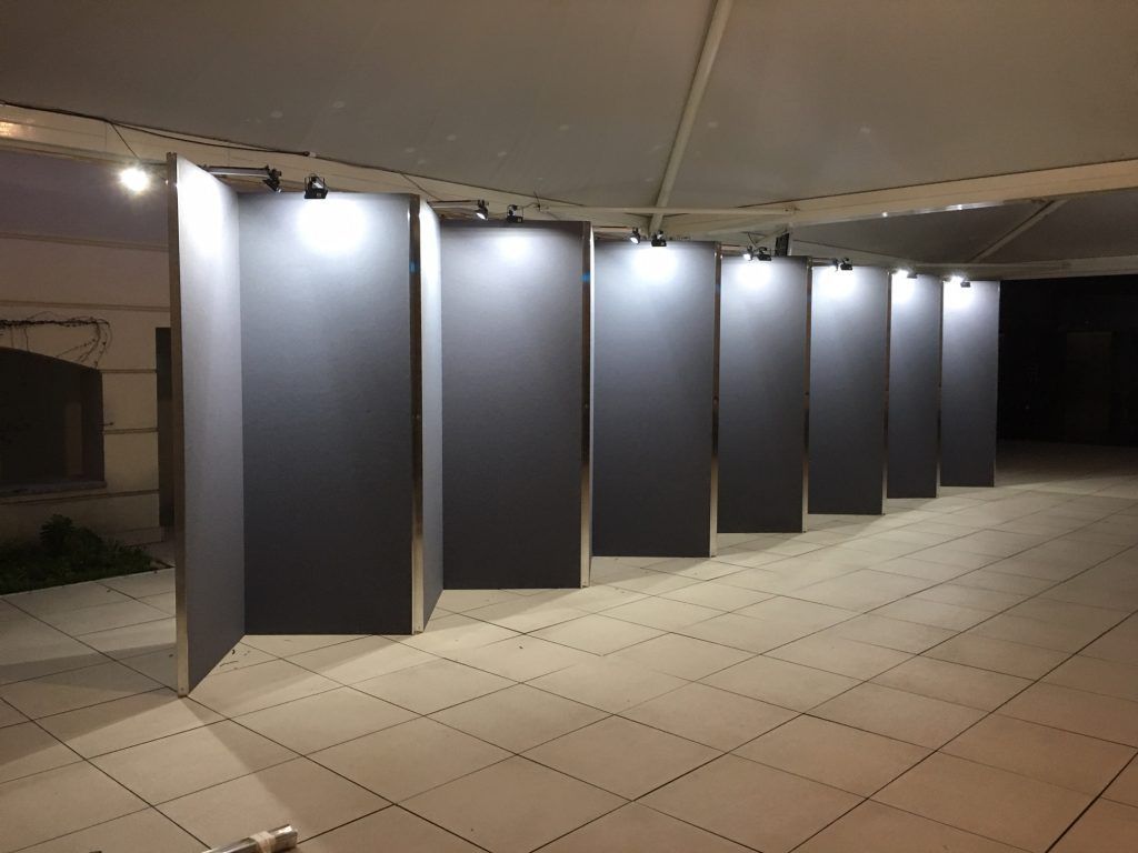 Una fila di pannelli espositivi illuminati sotto un passaggio coperto, di notte.