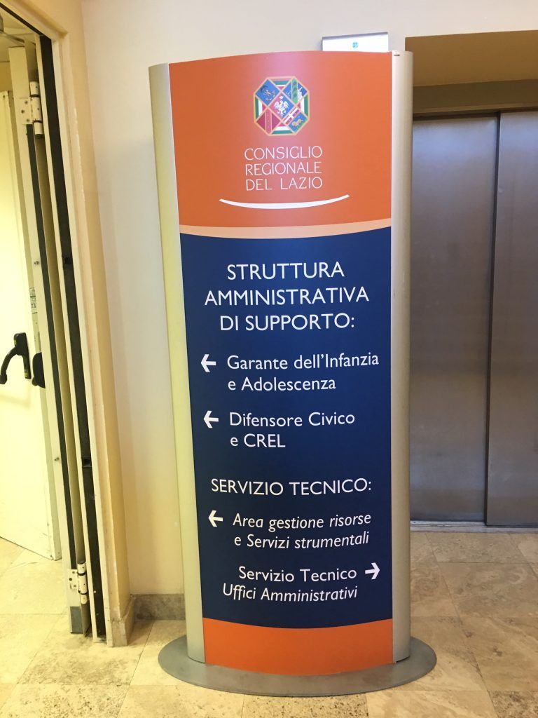 Segnaletica blu e arancione per il supporto amministrativo e i servizi tecnici in un corridoio.