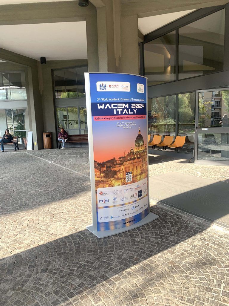 All'ingresso di un edificio è presente un cartellone pubblicitario blu che mostra uno scenario urbano al tramonto e la scritta 