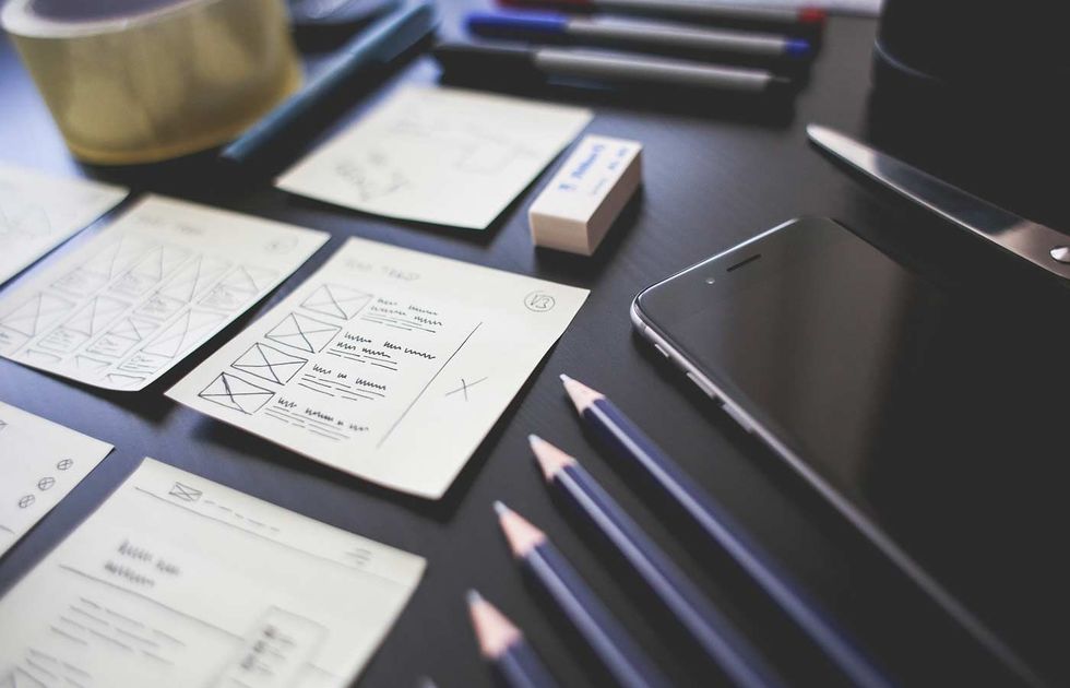 Scrivania con schizzi, matite, quaderno e smartphone su uno sfondo scuro.