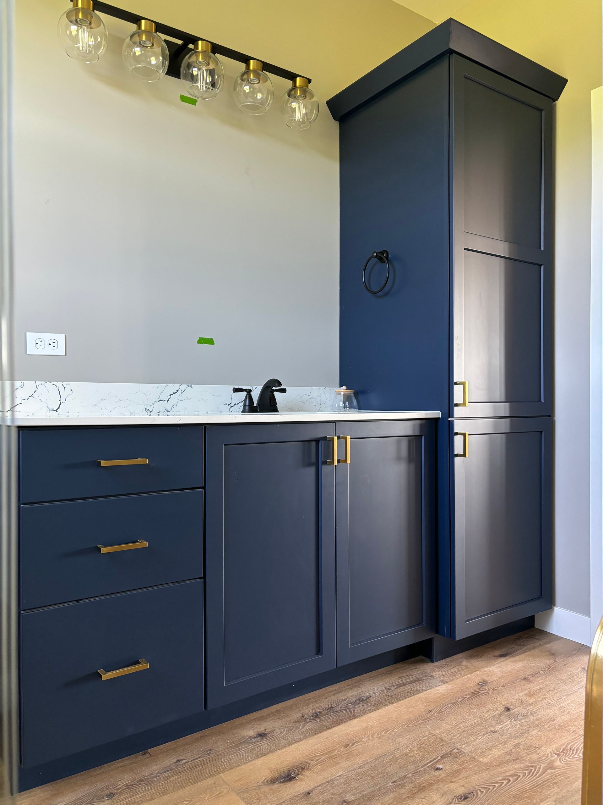 Navy blue bathroom vanity with drawers and cabinet, gold hardware, and a tall storage tower.