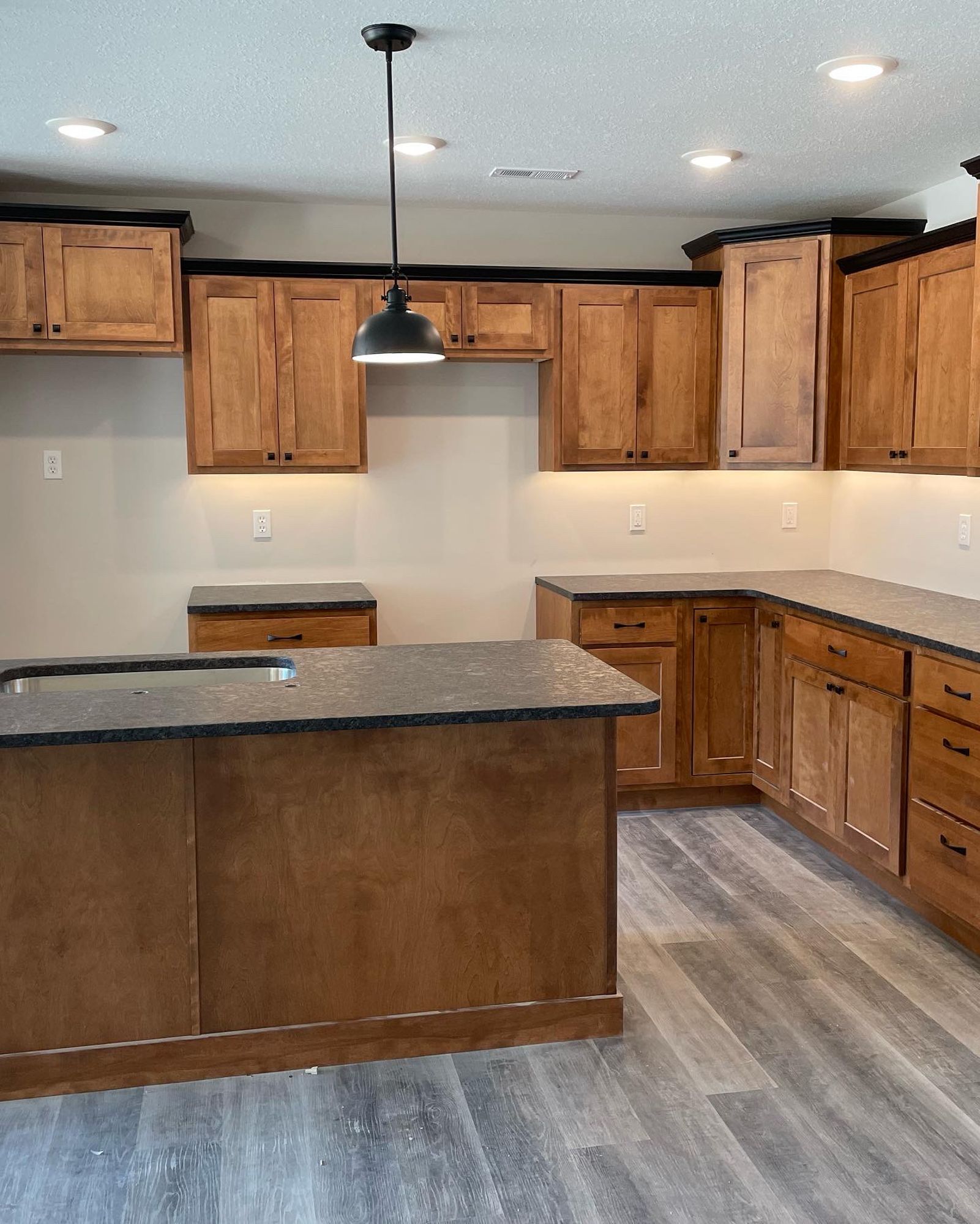 Wooden kitchen with island and overhead cabinets, gray countertops, and wood-look flooring.