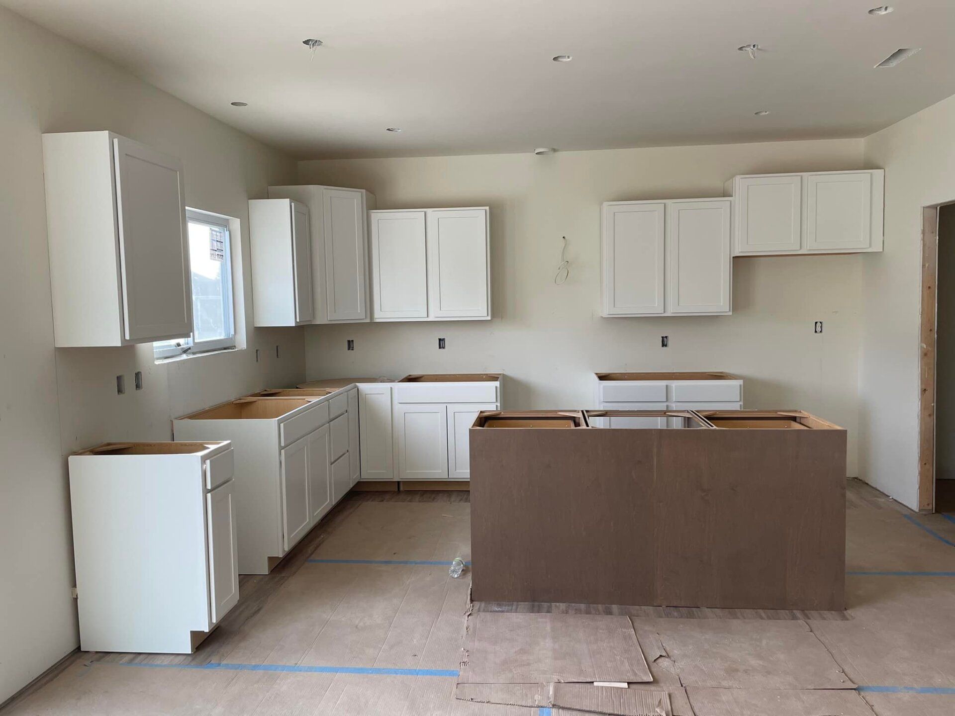 Unfinished kitchen with white cabinets, island, and window.