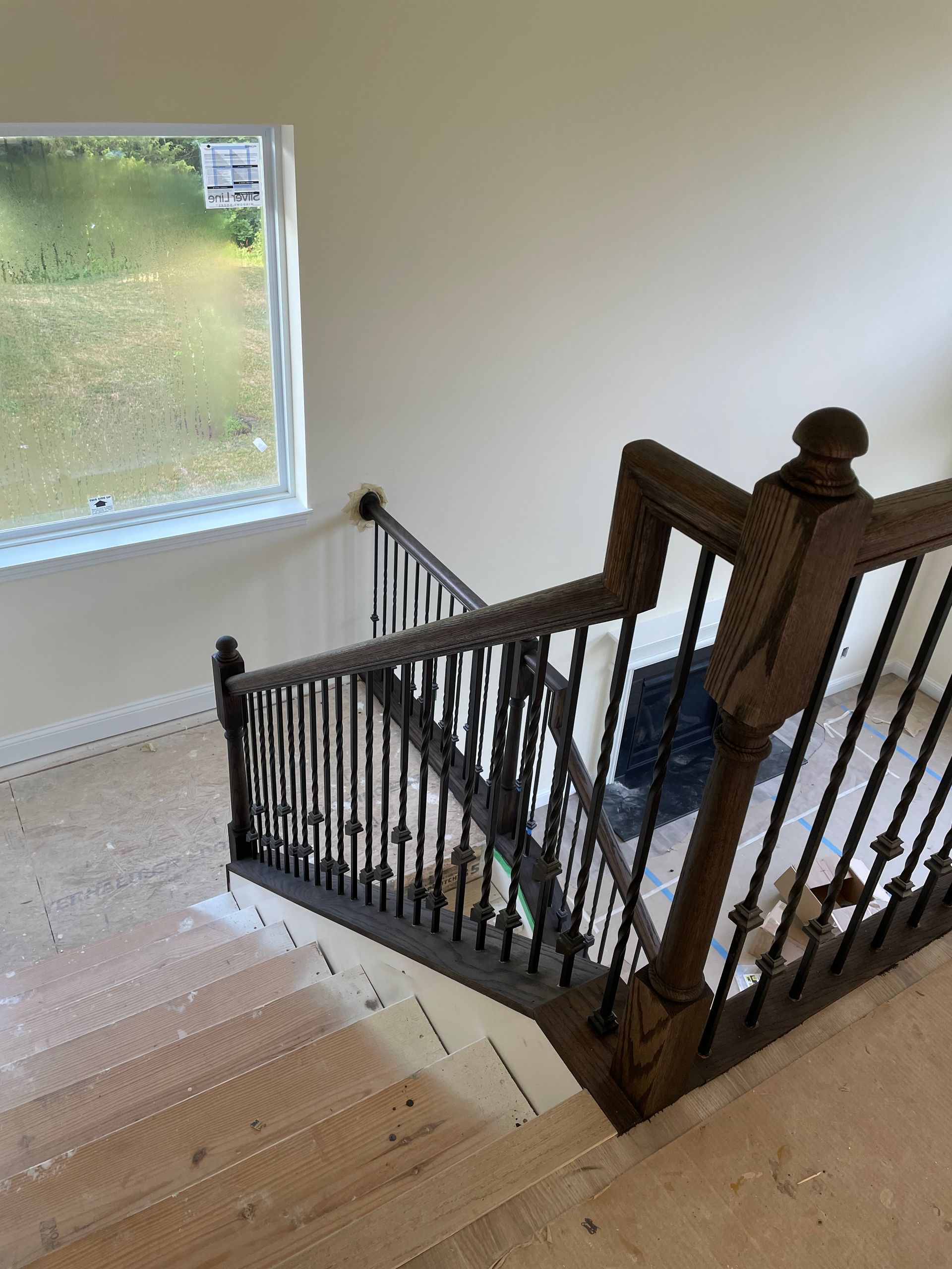 Staircase with wooden handrail and black metal balusters; a window in the background.