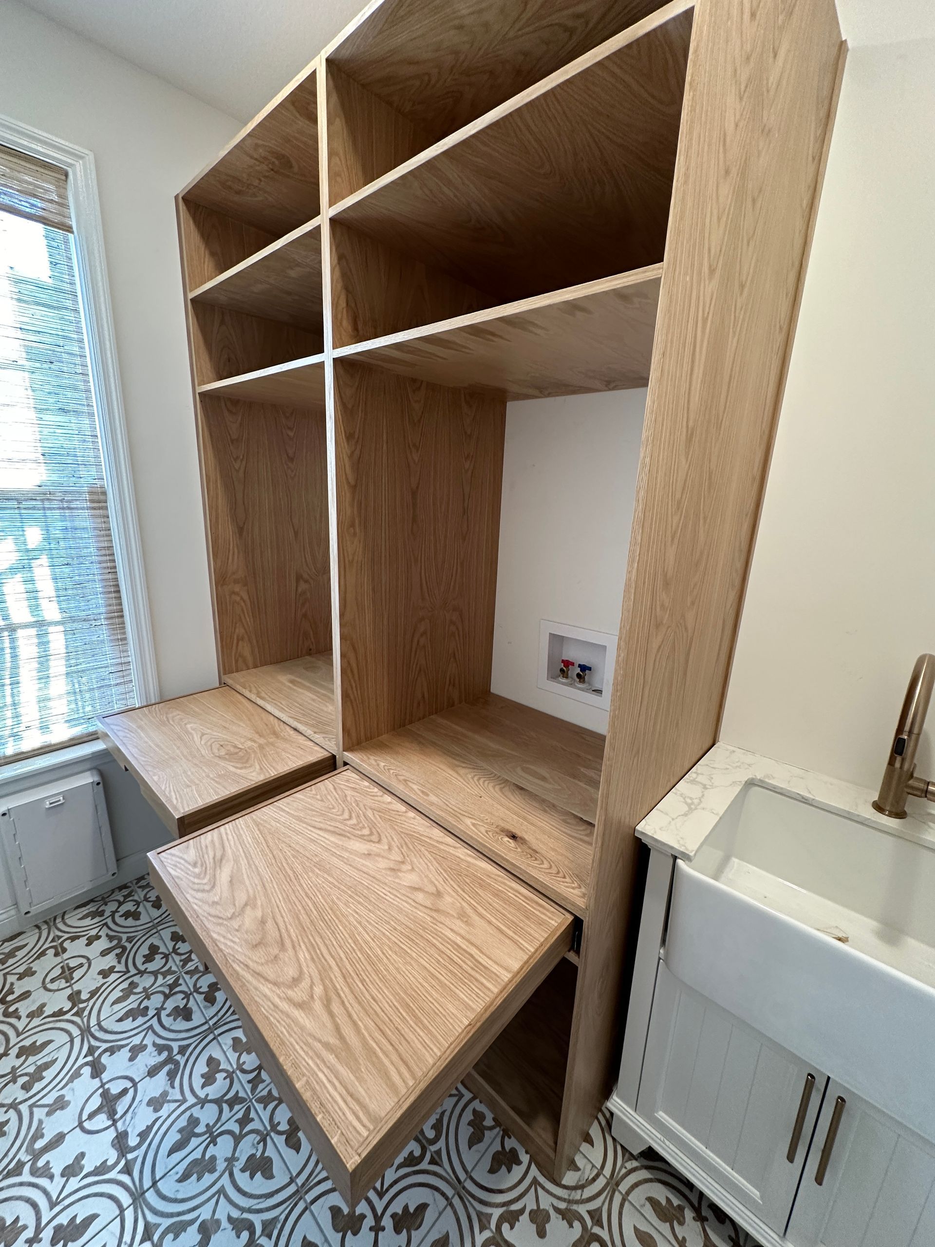 Custom built-in wooden shelving unit with pull-out desks, next to a window and a sink.
