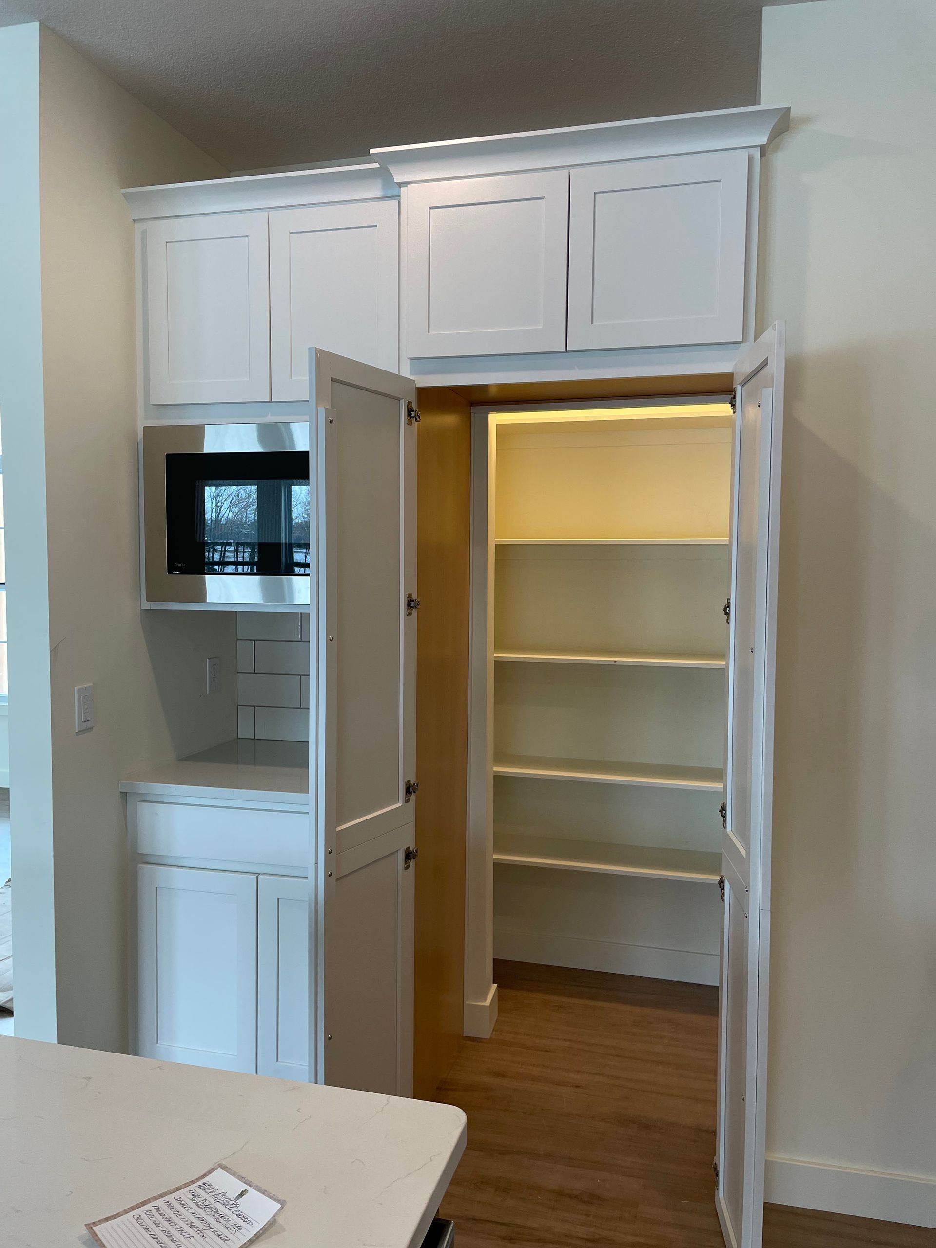 White pantry cabinet with open doors revealing shelves, microwave, and storage.