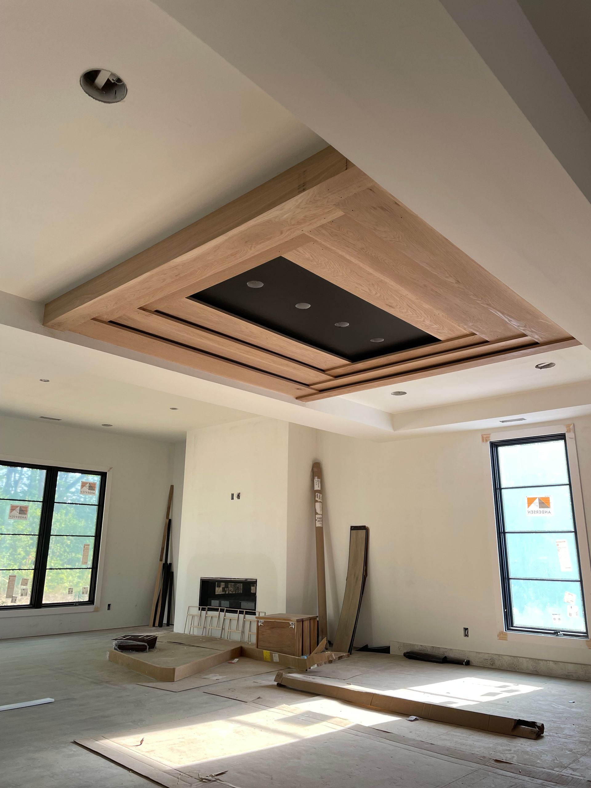 Room under construction with a multi-layered wood and black ceiling feature and large windows.