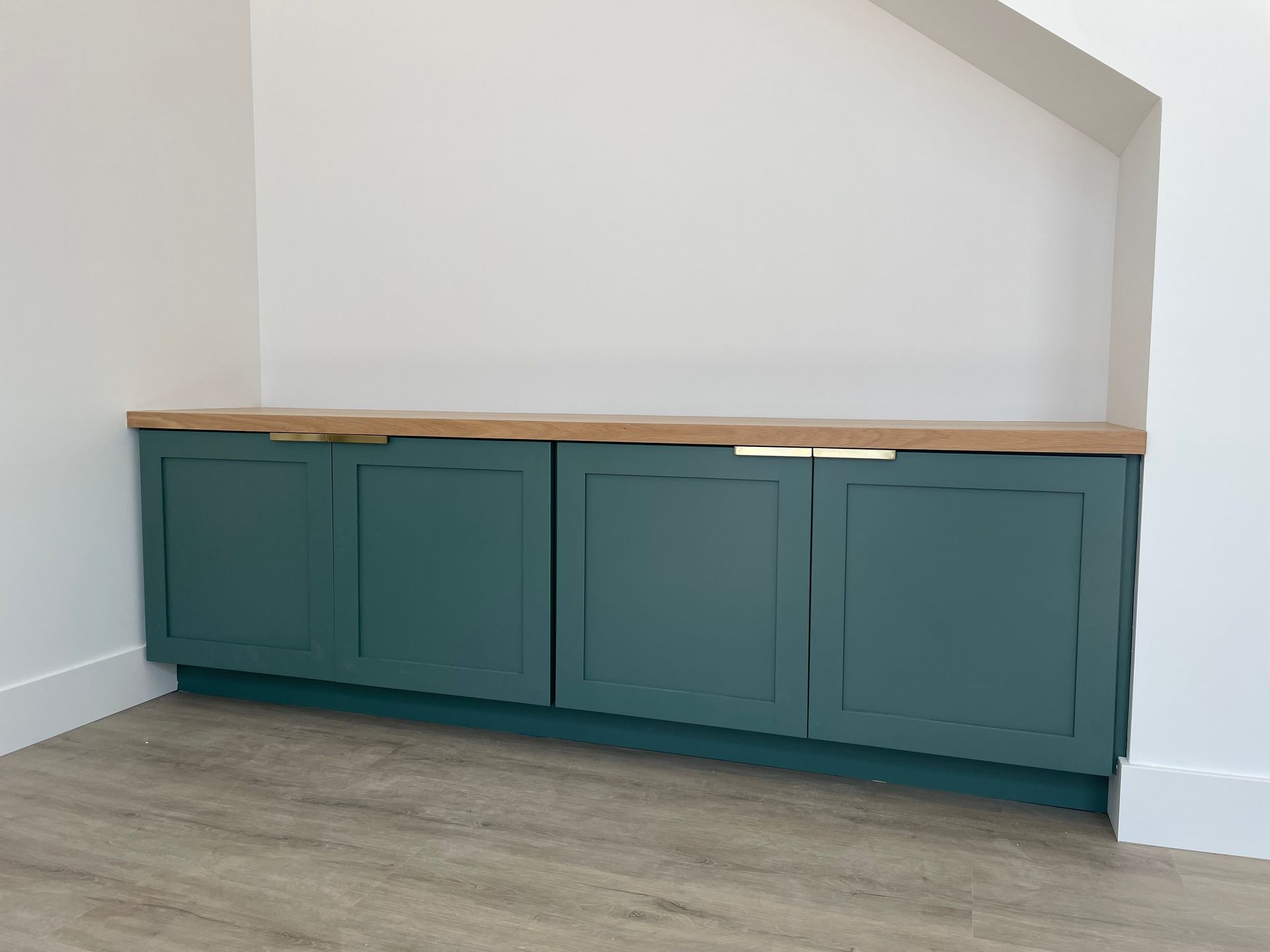 Green cabinets with a wooden countertop against a white wall and a light-colored floor.