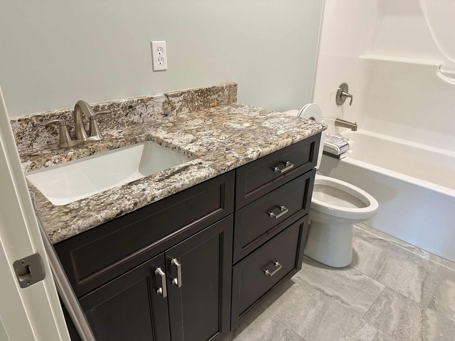 Bathroom with dark brown vanity, granite countertop, white sink, and bathtub.