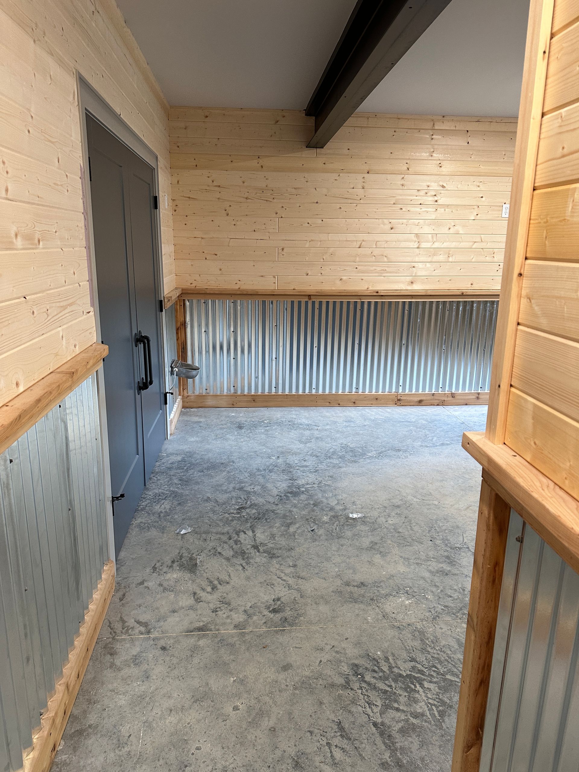 Interior with concrete floor, corrugated metal wainscoting, light wood paneling, dark gray door.