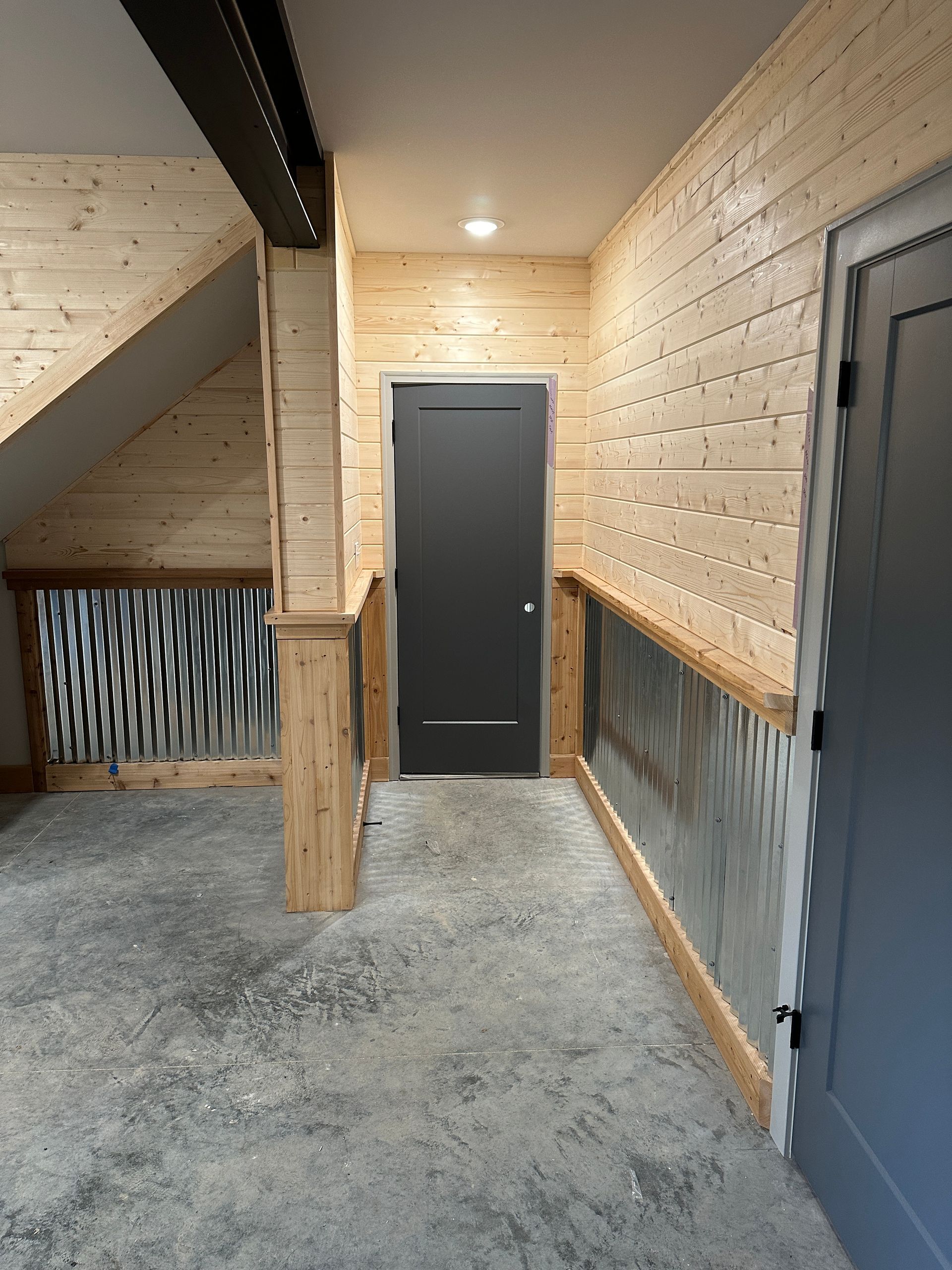 Corrugated metal and wood railing in hallway, gray door at the end.