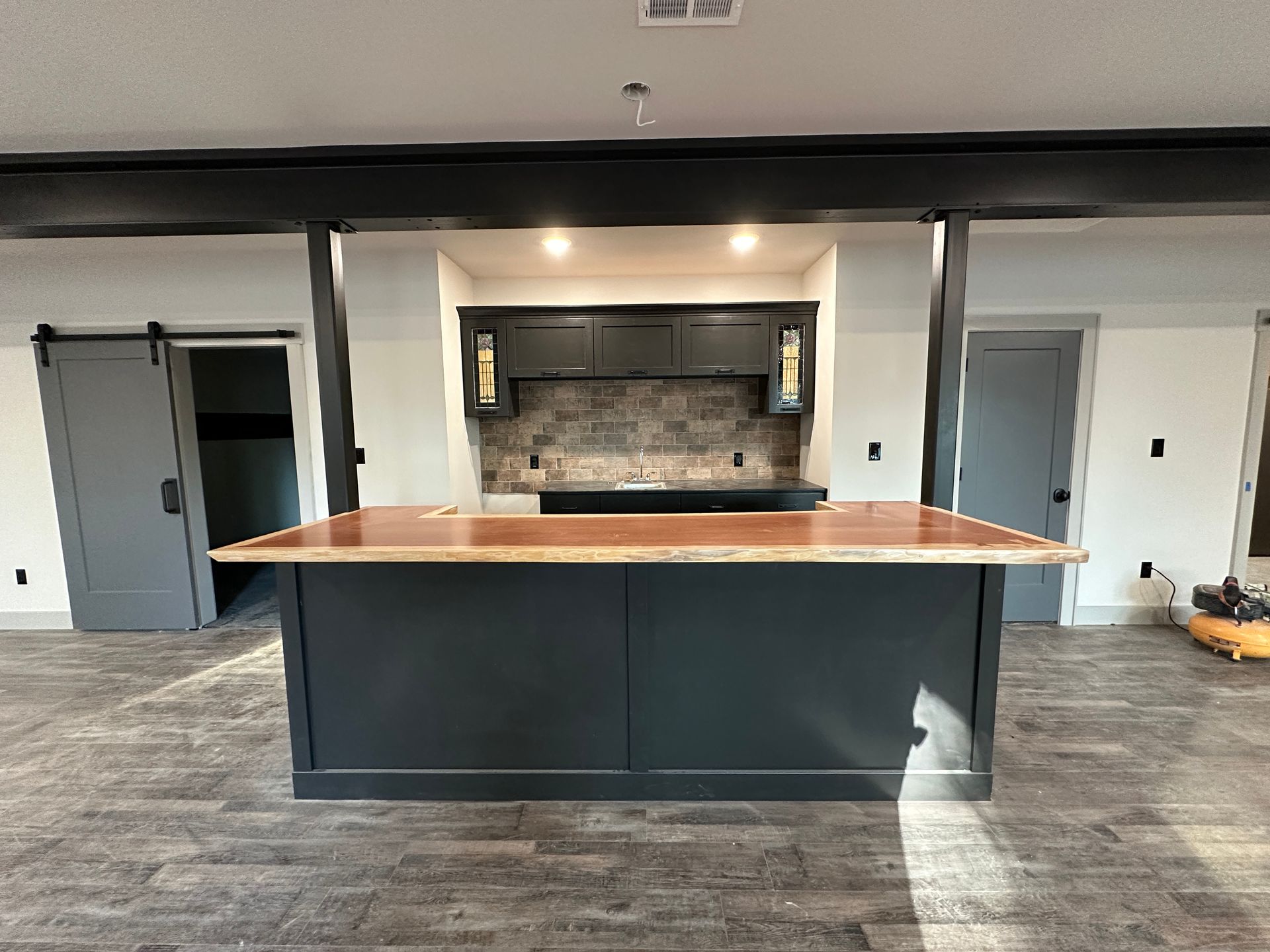 Dark blue kitchen island with natural wood countertop, black cabinets and doors in a modern kitchen.