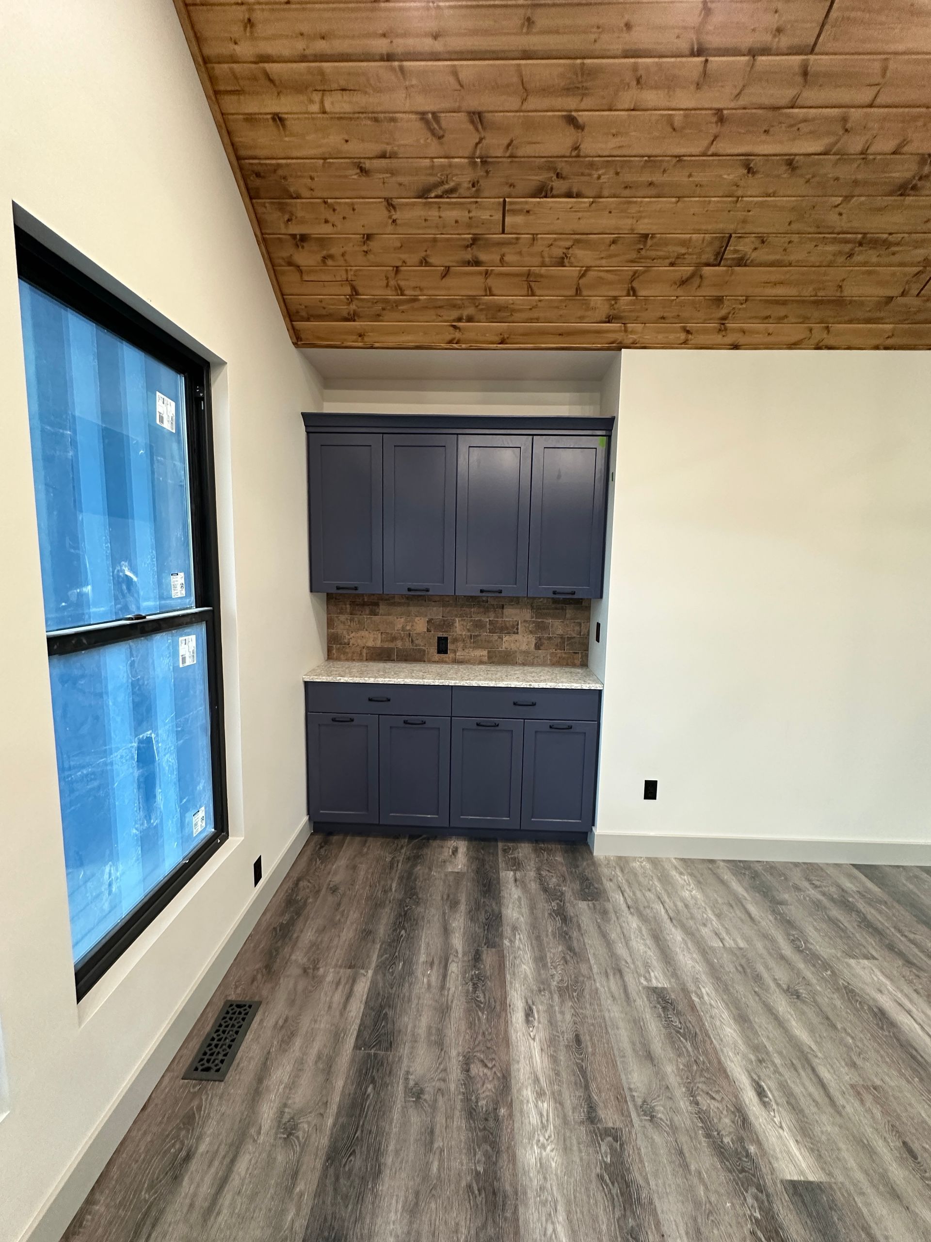 Interior with blue cabinets, wood ceiling, large window, and gray flooring.