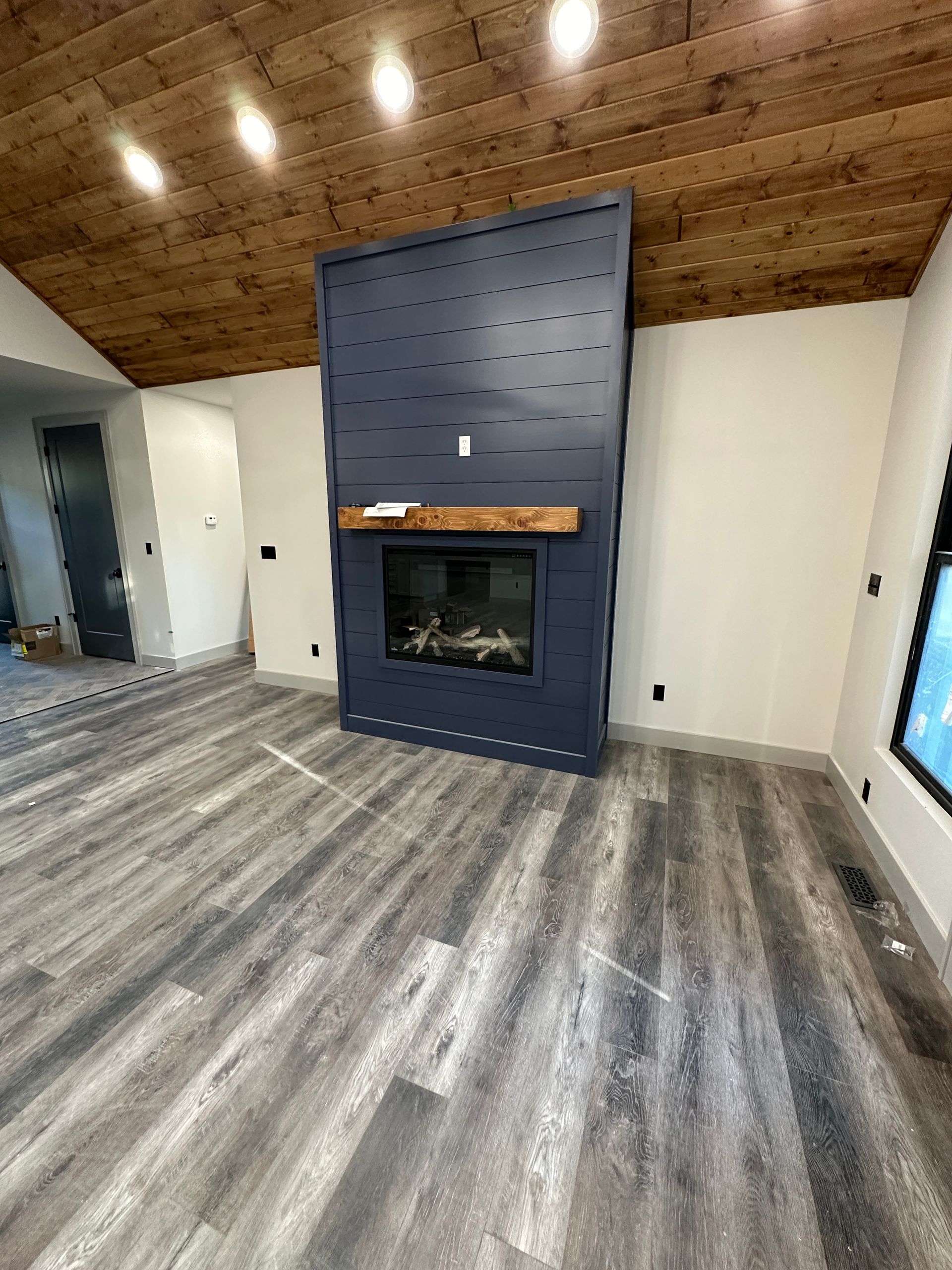 A modern living room with a blue fireplace, wood ceiling, and grey floors.