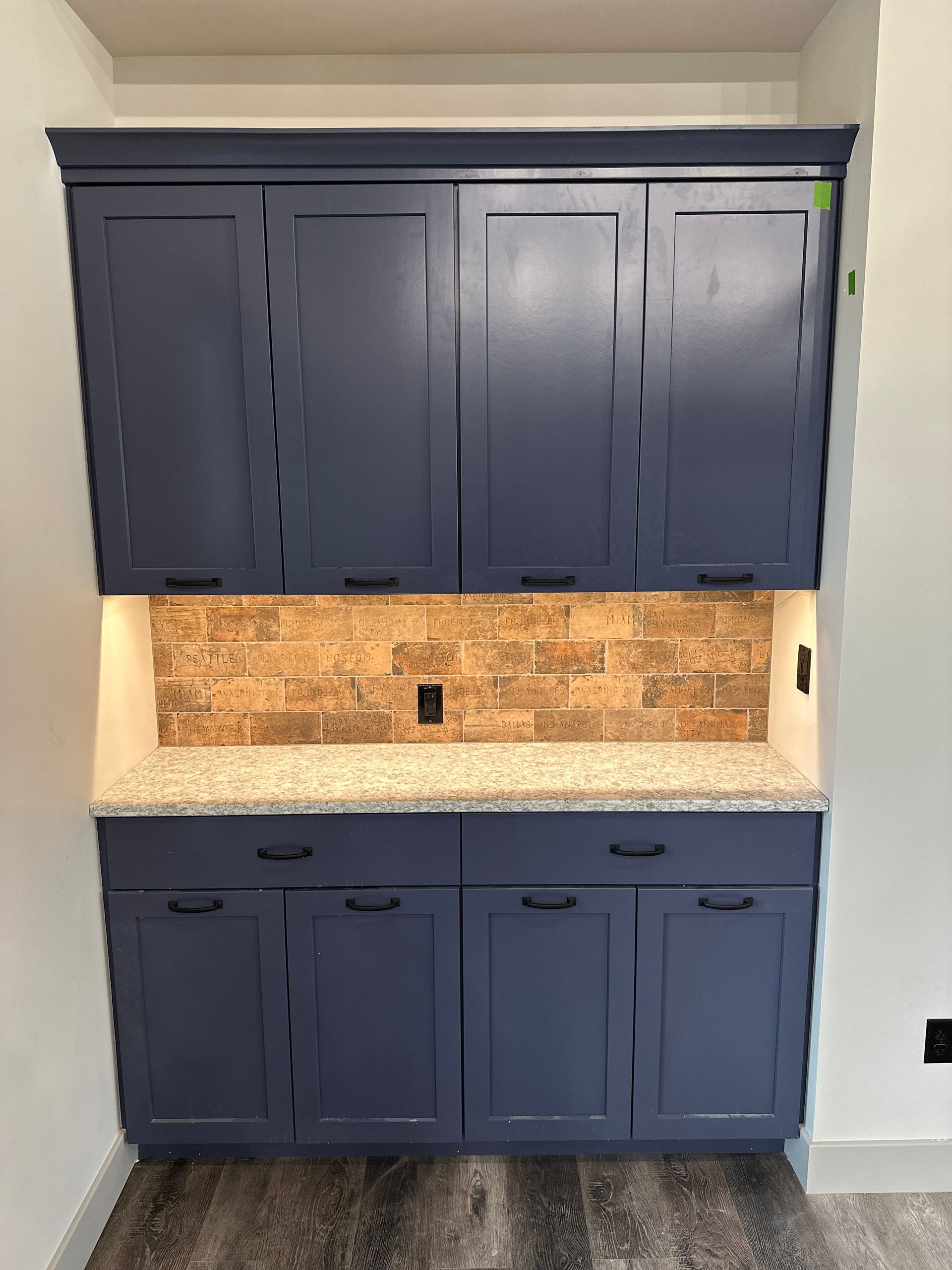Built-in navy blue cabinets with a granite countertop, brick backsplash, and under-cabinet lighting.