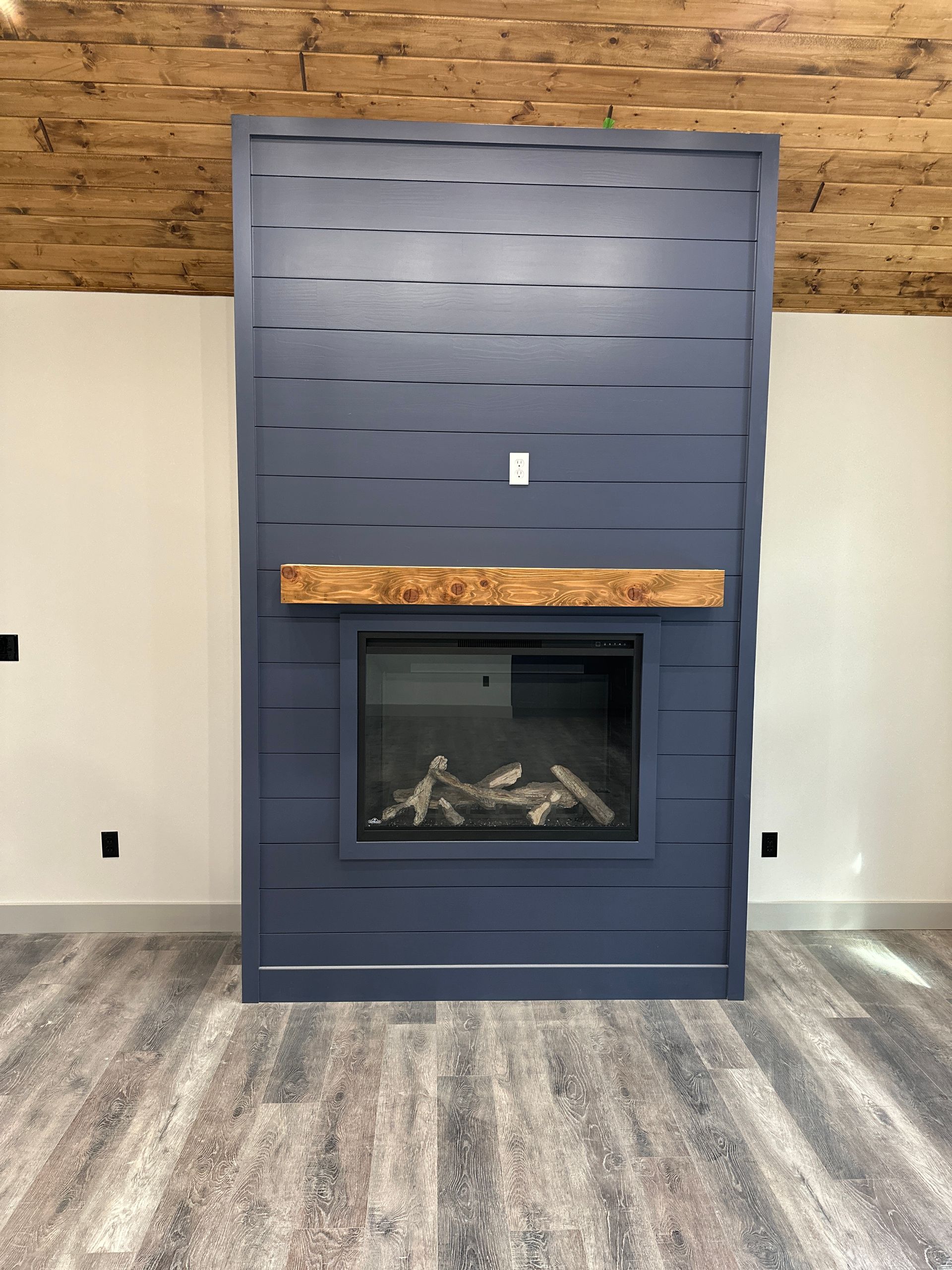 Blue accent wall with fireplace, wooden mantle, and wood-paneled ceiling.