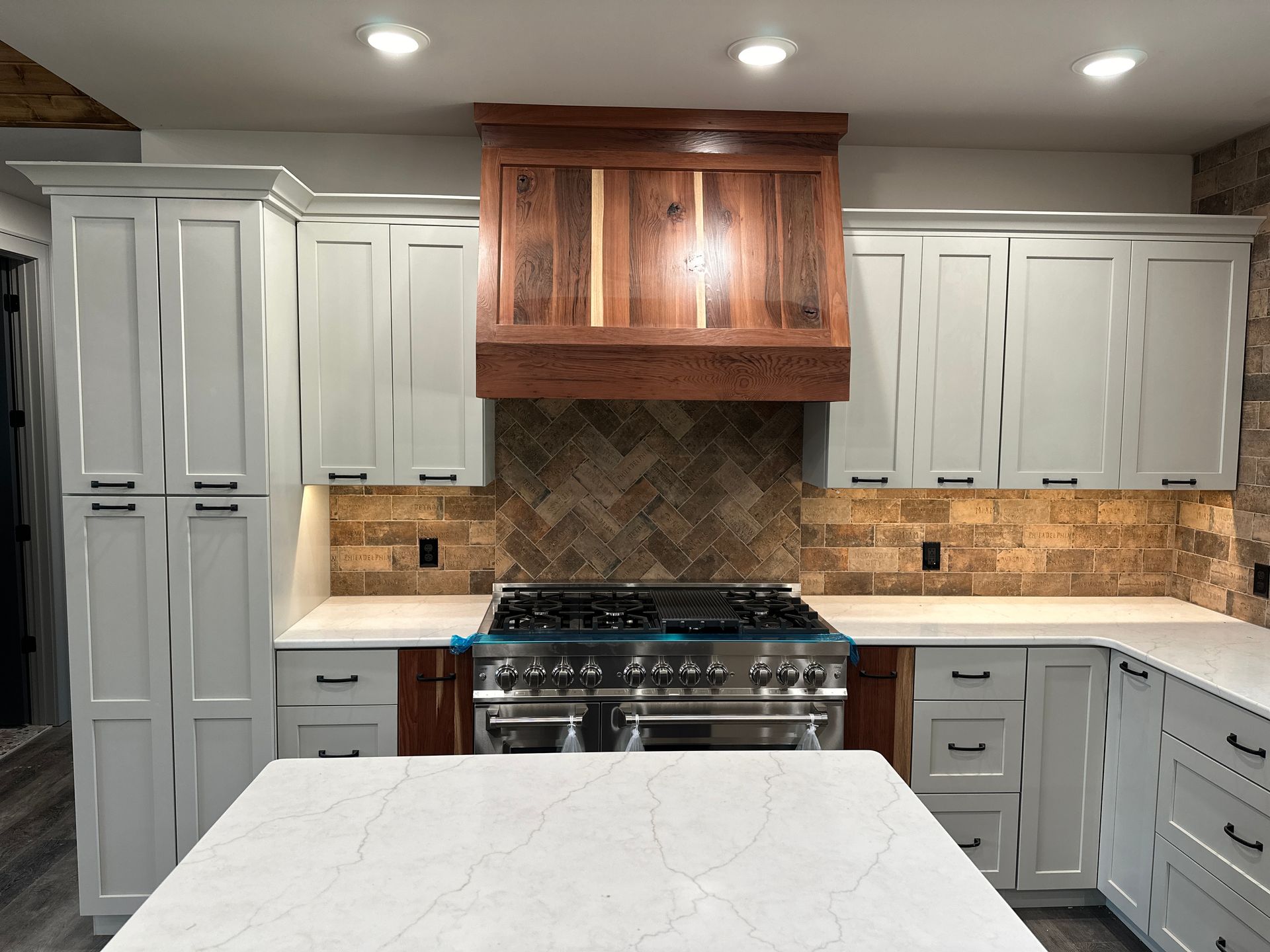 Kitchen with gray cabinets, wood range hood, and white countertops.