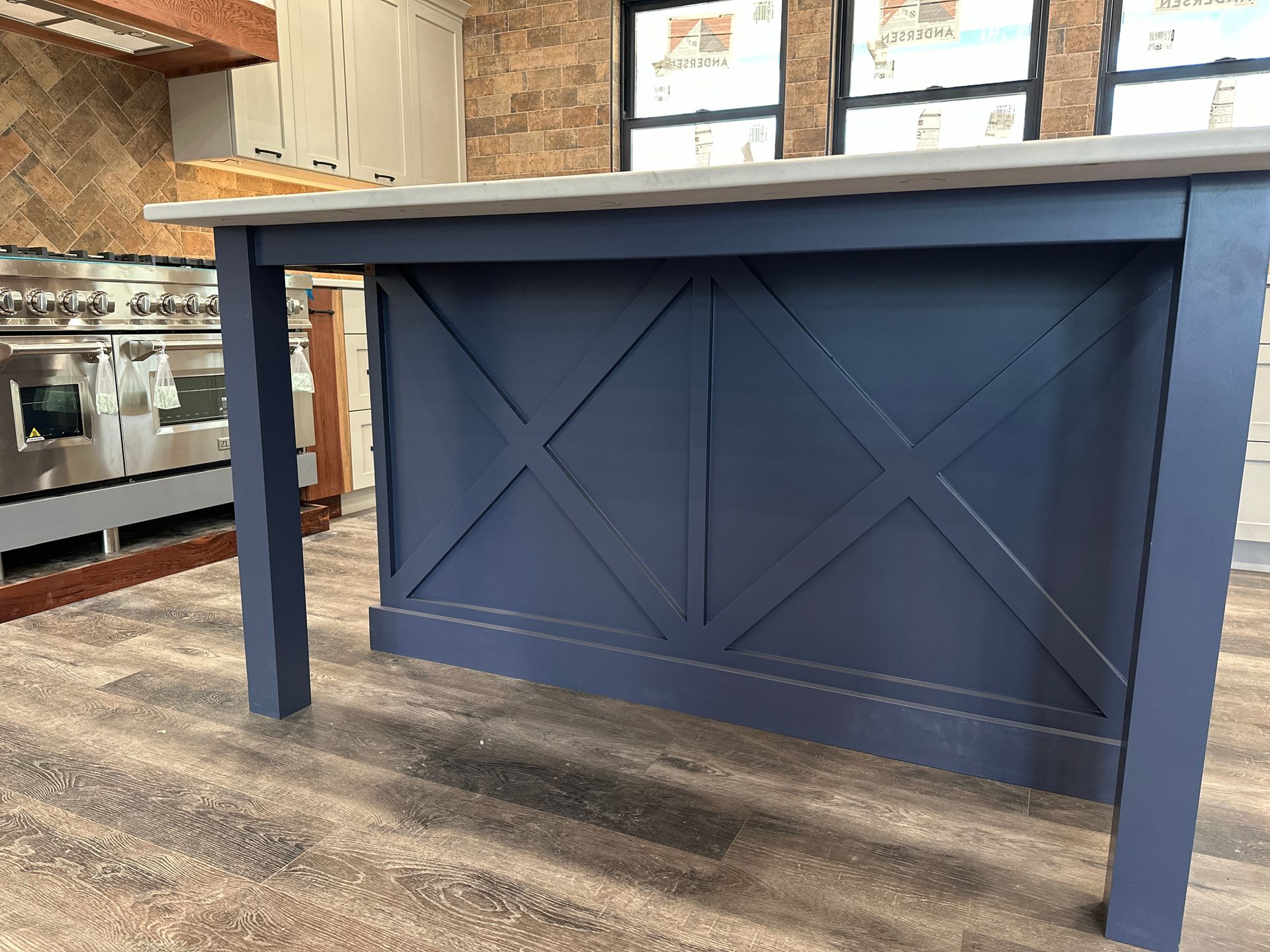Blue kitchen island with an X design, gray countertop, and wood flooring.