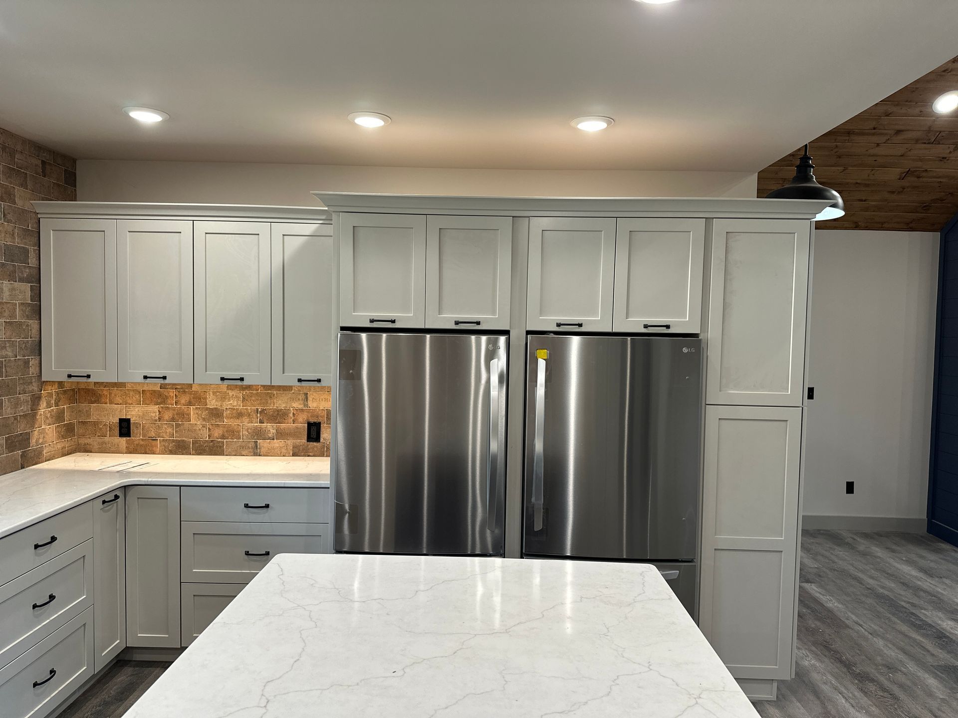 Modern kitchen with white cabinets, stainless steel refrigerator, and stone backsplash.