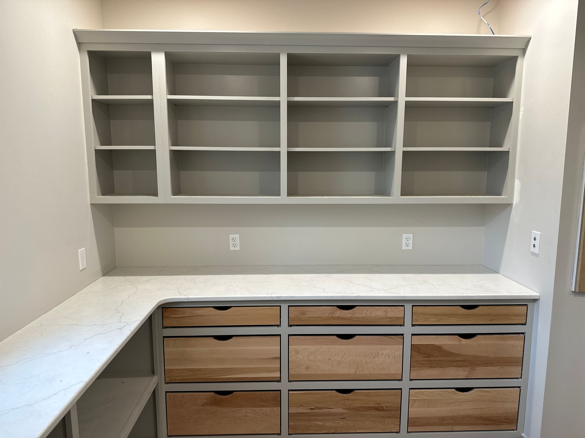 Built-in pantry with gray shelving and light wood drawers beneath a white countertop.