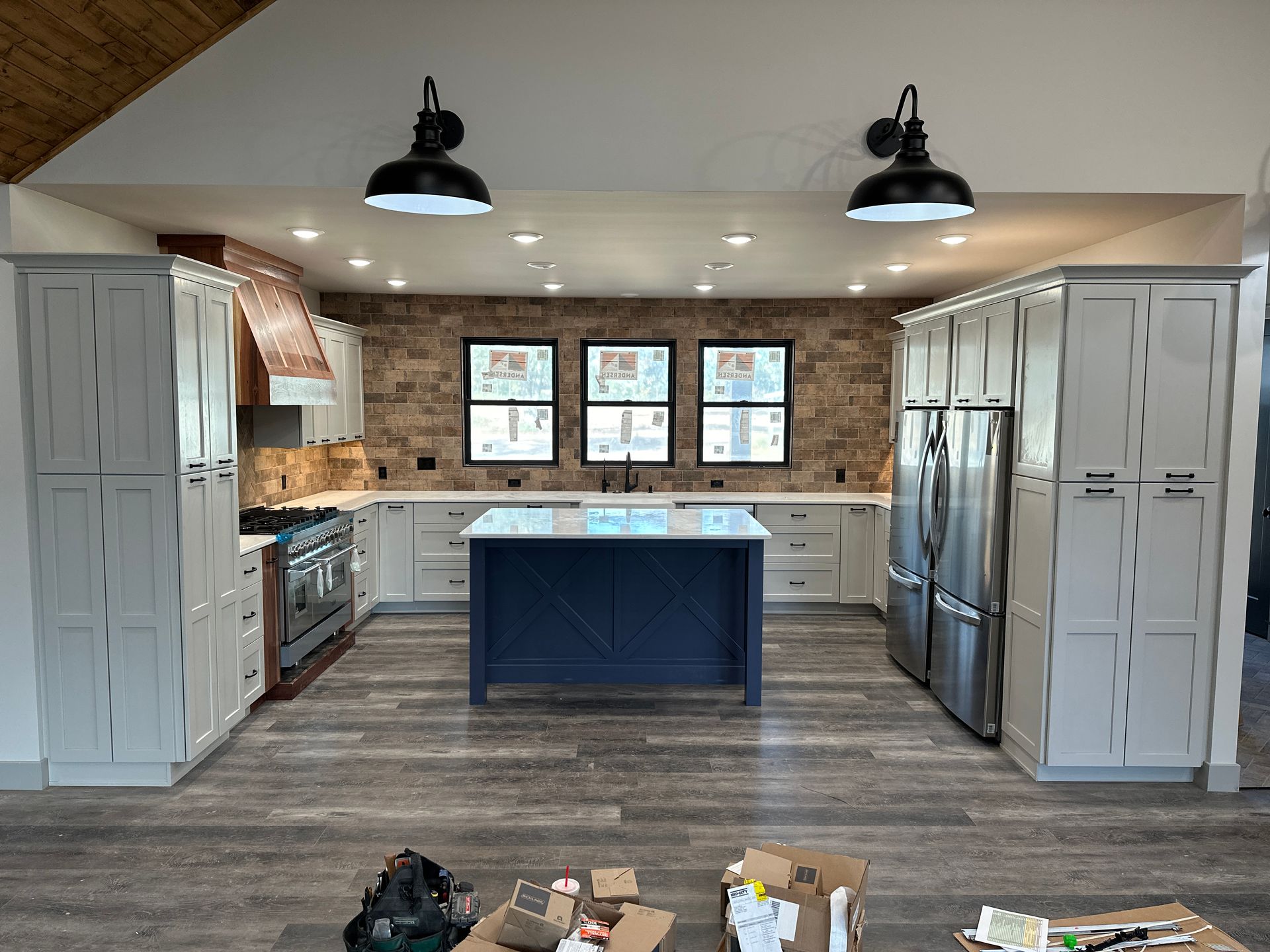 Modern kitchen with light gray cabinets, brick backsplash, dark blue island, stainless steel appliances, and wood-look flooring.