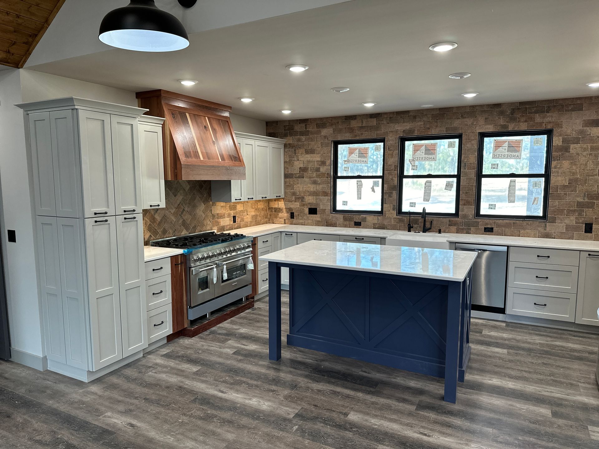Modern kitchen with light gray cabinets, blue island, brick wall, and stainless steel appliances.