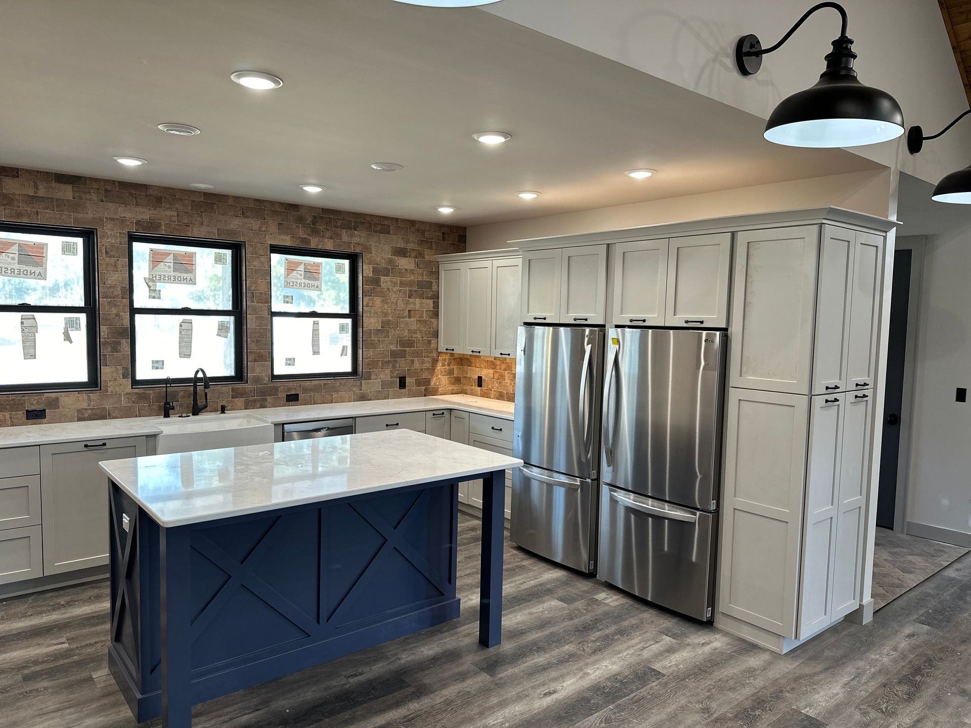 Modern kitchen with blue island, stainless steel fridge, white cabinets, and brick accent wall.