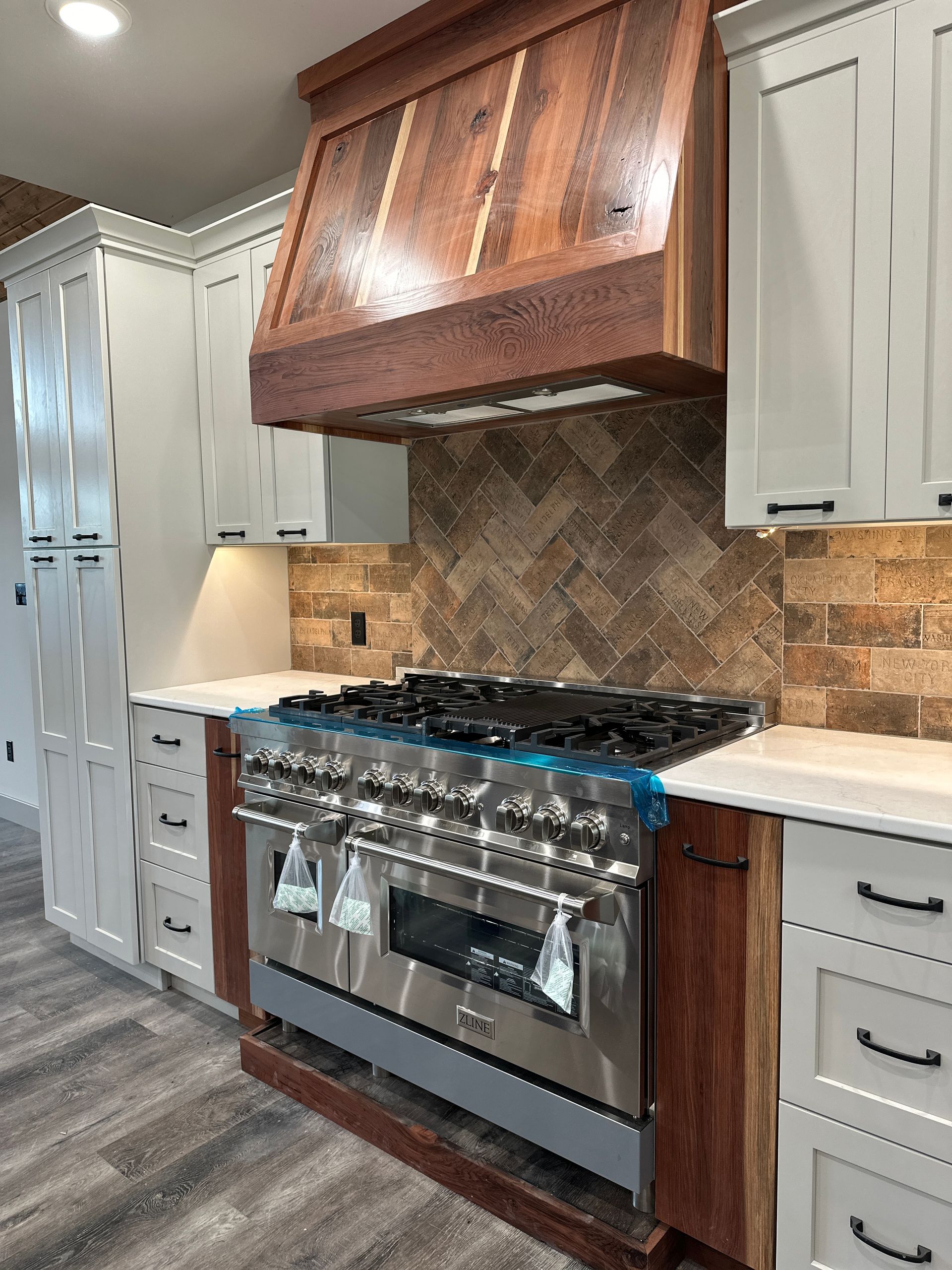 Kitchen with stainless steel range, wood hood, light-colored cabinets, and brown tile backsplash.