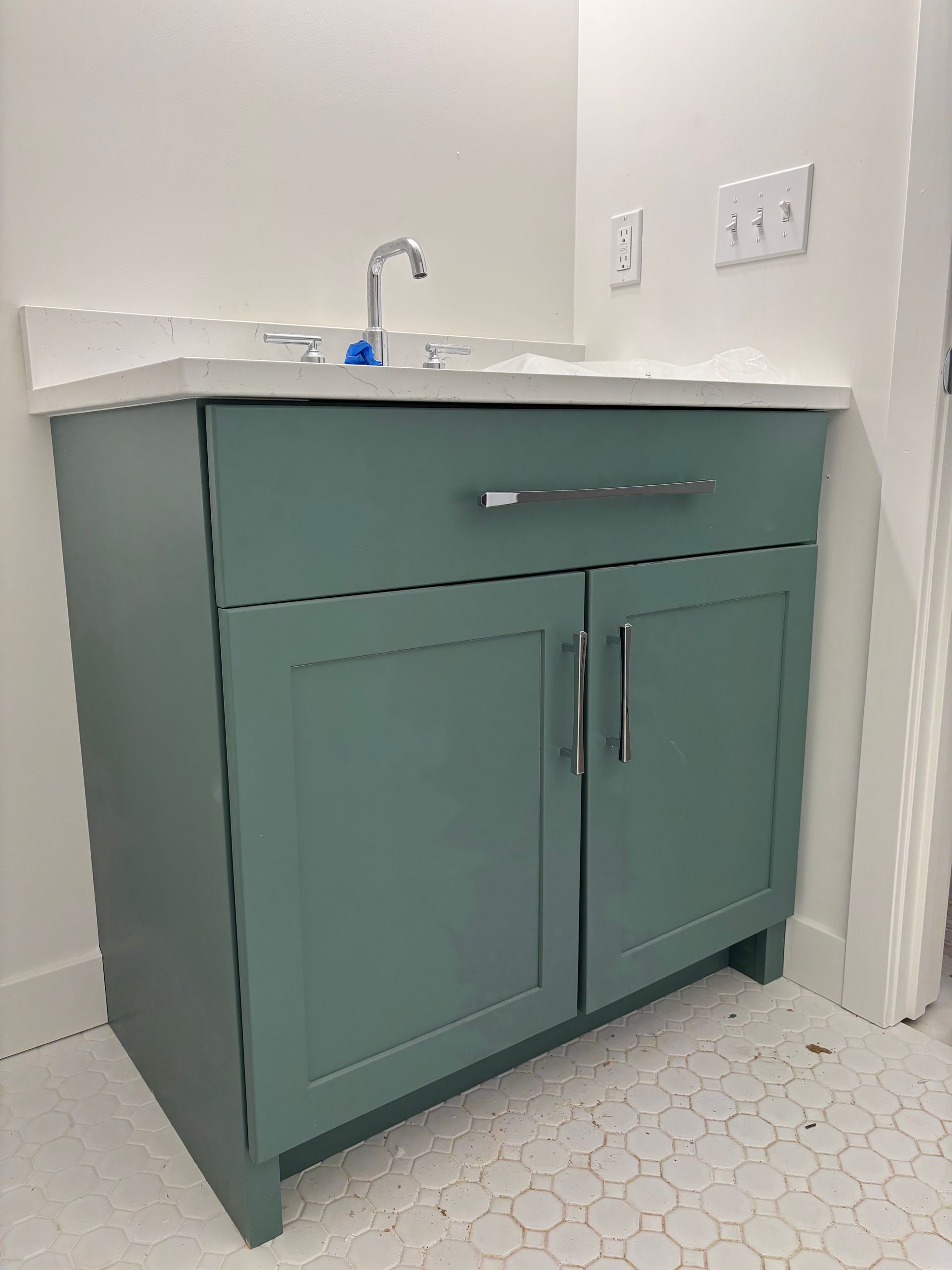 Green bathroom vanity with a white countertop and silver faucet in the corner of a room.