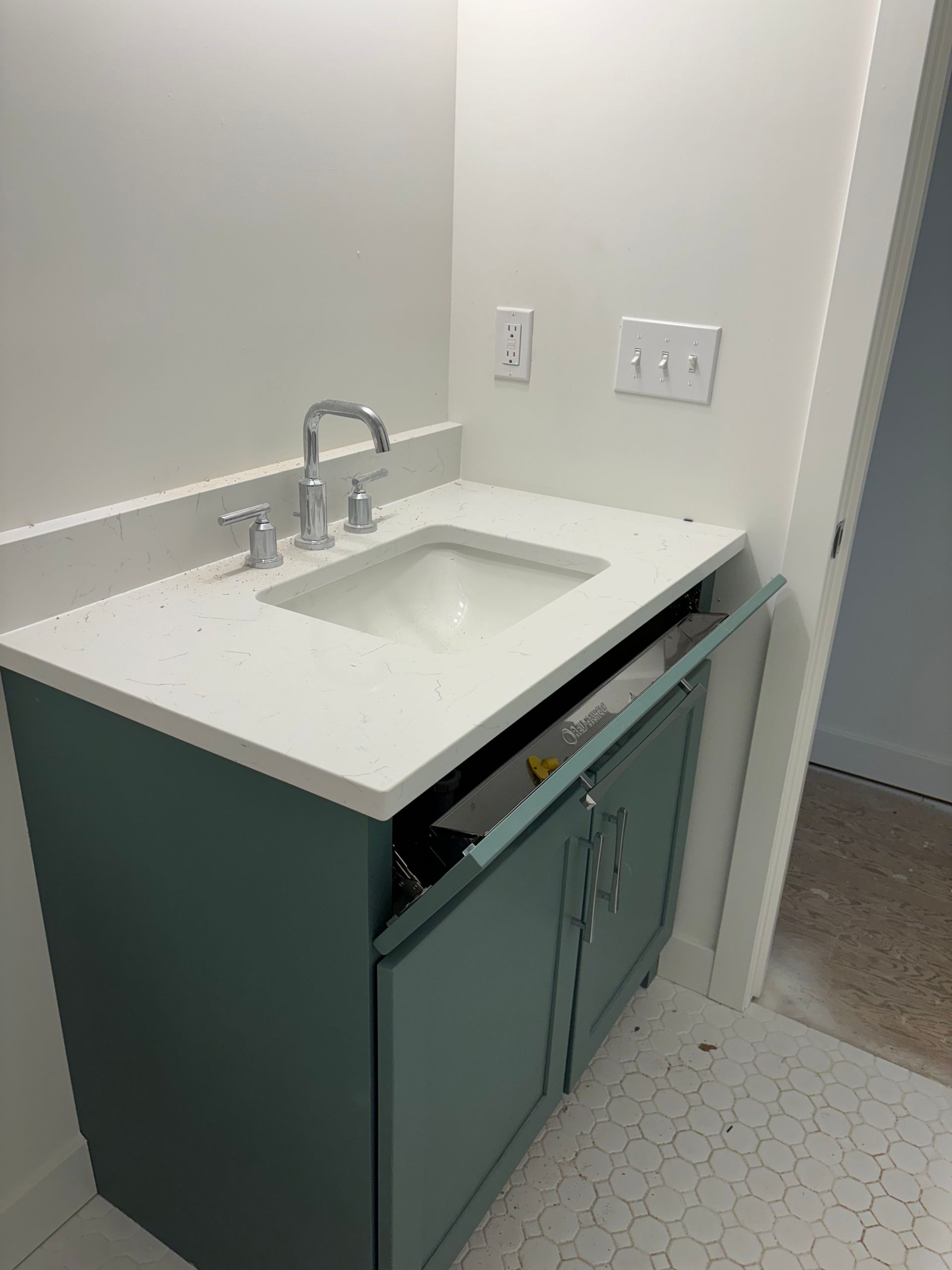 Teal bathroom vanity with partially open door, white countertop, sink, chrome faucet, and outlets.