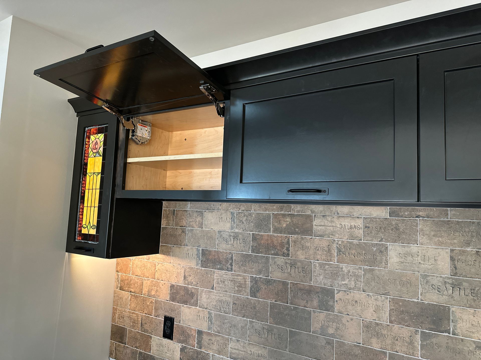 Black kitchen cabinets, one open, above a brick backsplash.