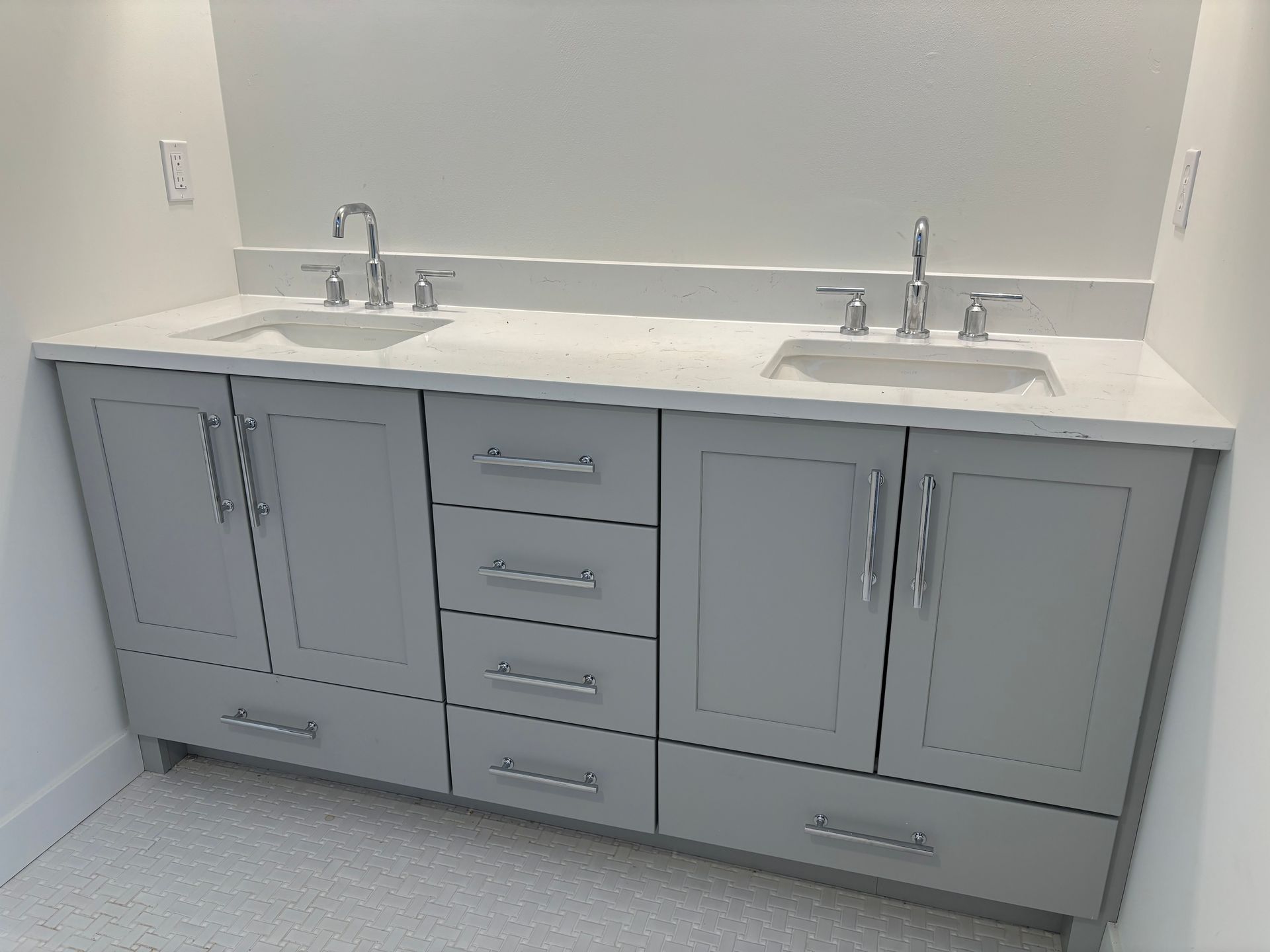Gray double vanity with white countertop, two sinks, and chrome faucets in a bathroom.
