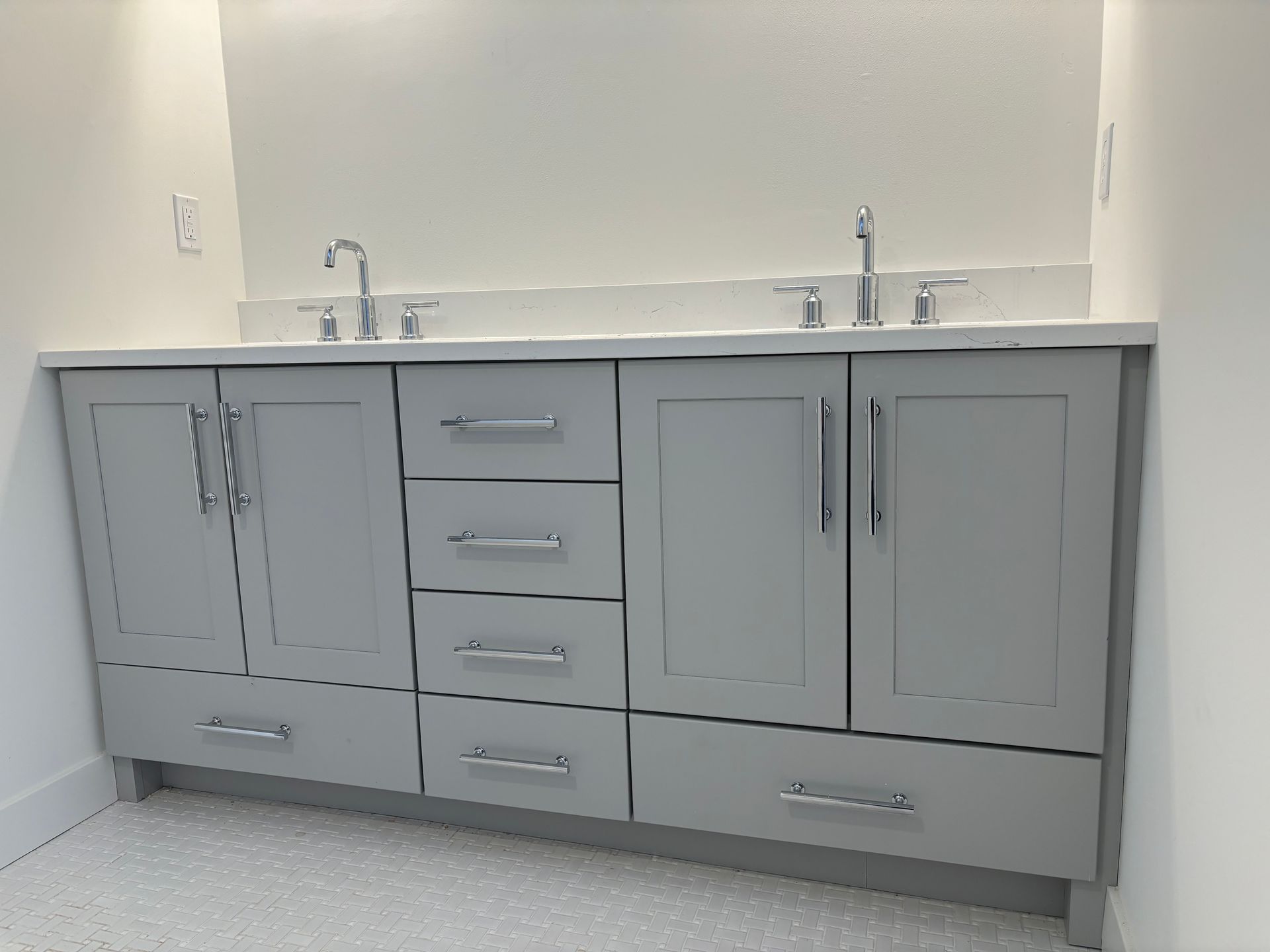 Gray double sink vanity with chrome fixtures and white countertop against a white wall.