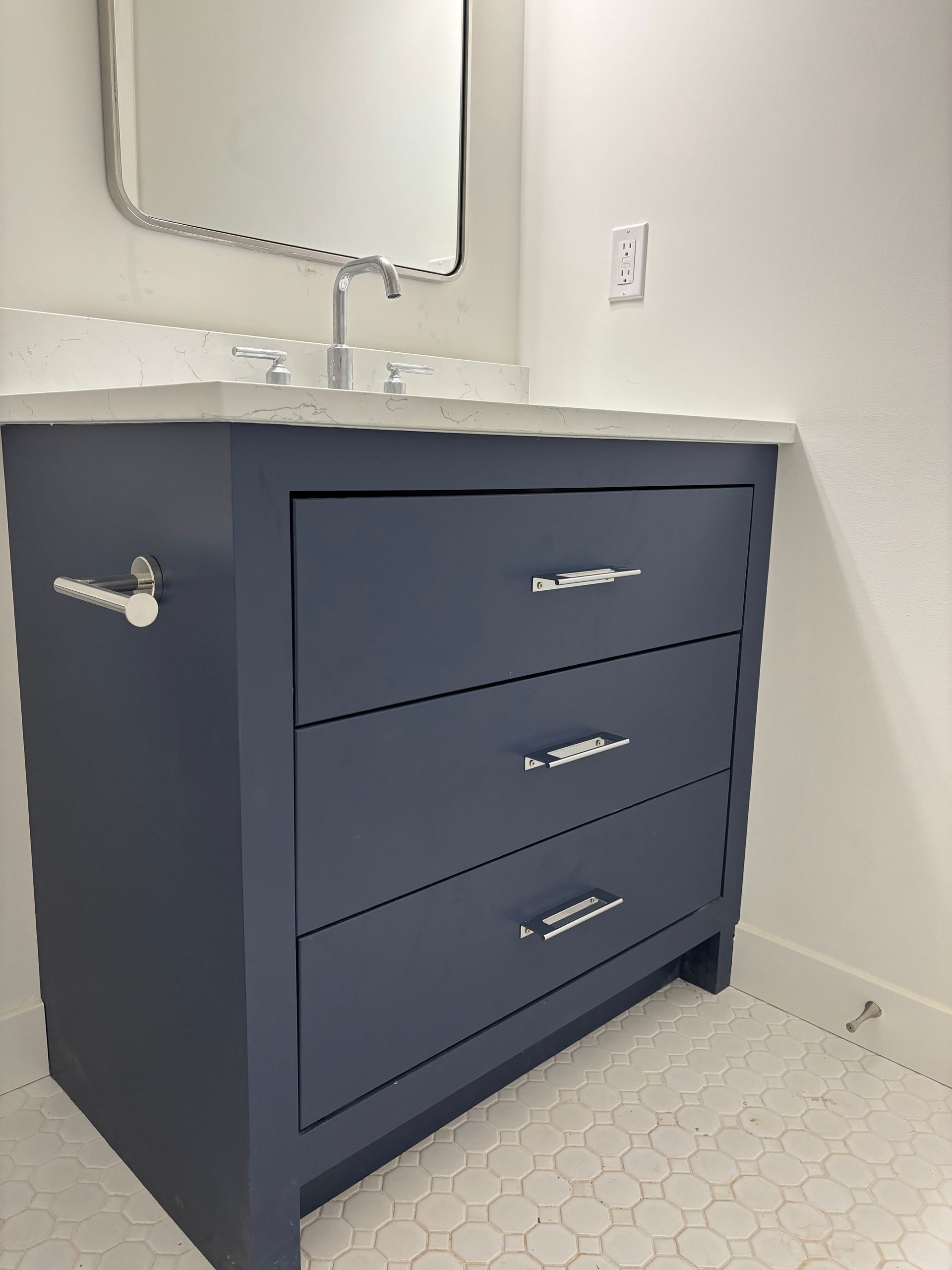 Blue bathroom vanity with three drawers, chrome hardware, white countertop, and scalloped mirror.