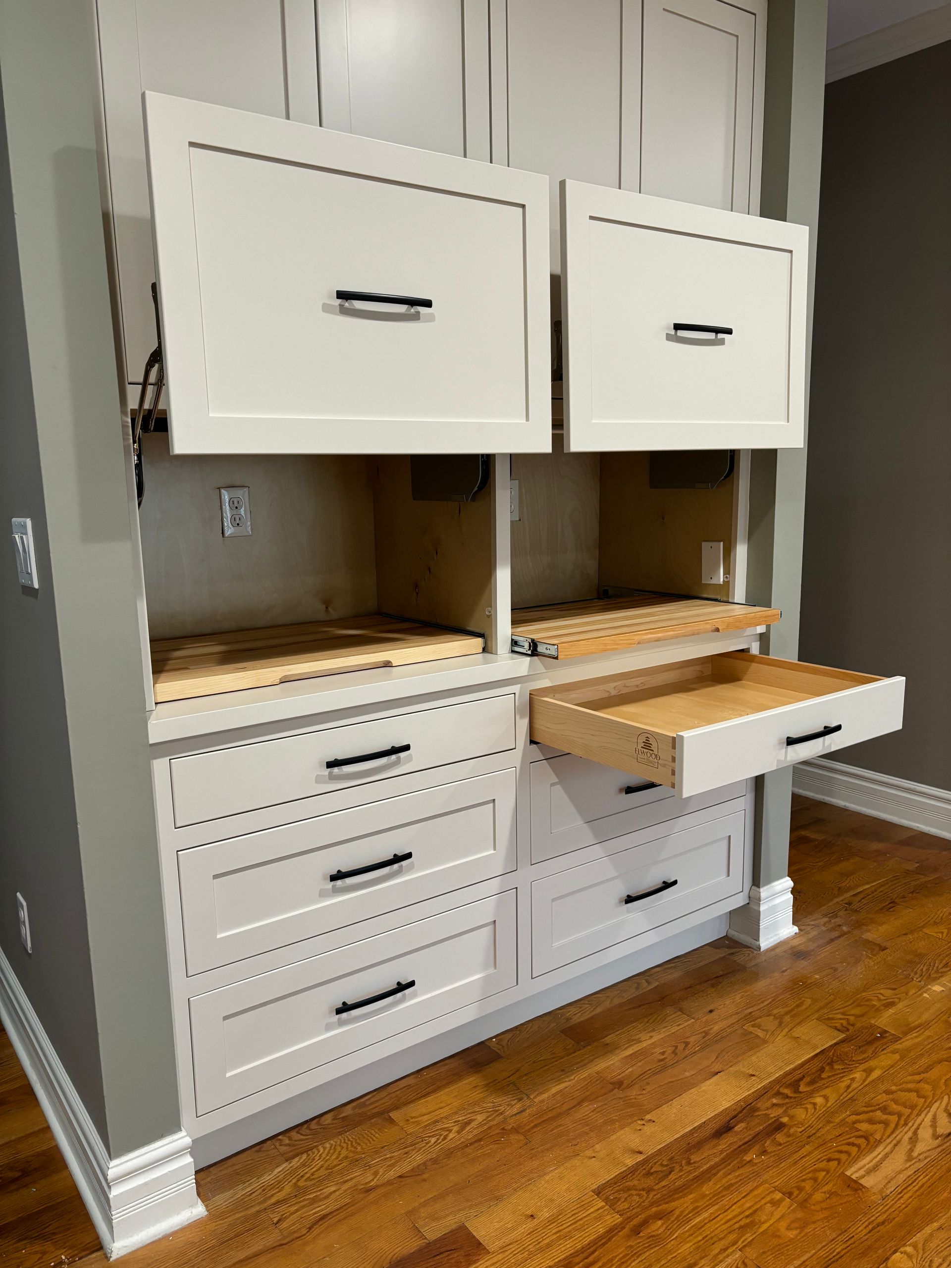 White built-in cabinetry with open top doors, drawers, and wooden shelves; grey walls and wood floors.